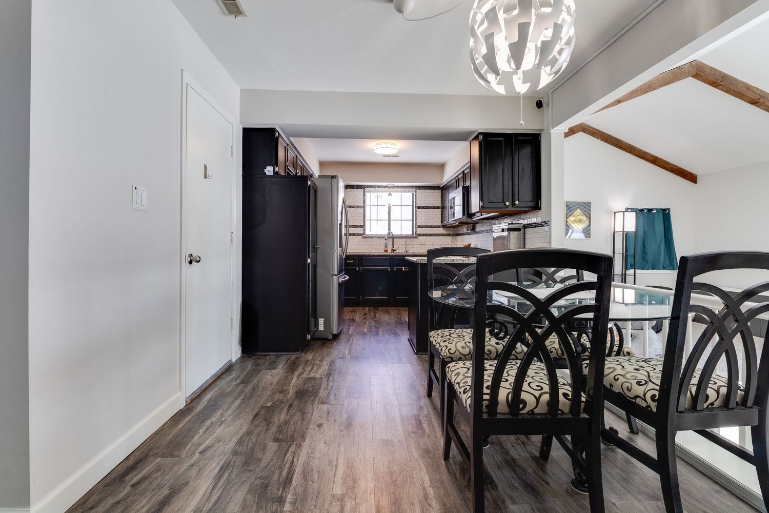 Modern dining area with black chairs and wood flooring connecting to a sleek kitchen space.