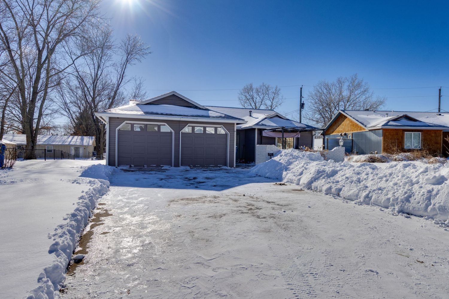 Snow-covered driveway leads to a white house with attached garage on a sunny winter day.