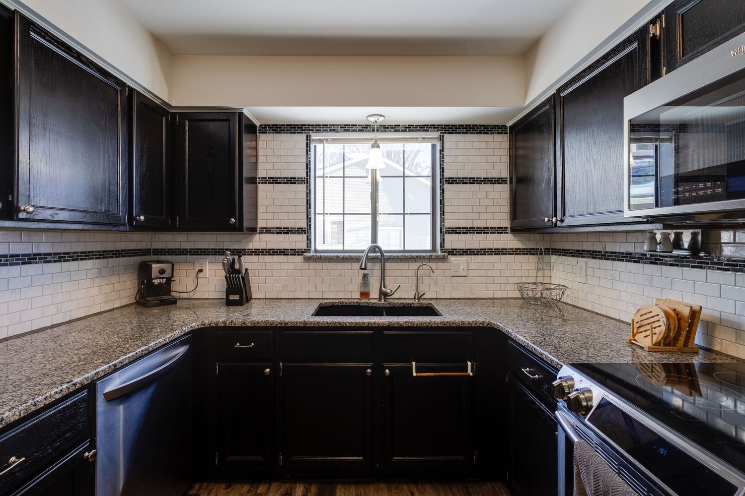 Modern kitchen with black cabinets, granite countertops, and subway tile backsplash around window.