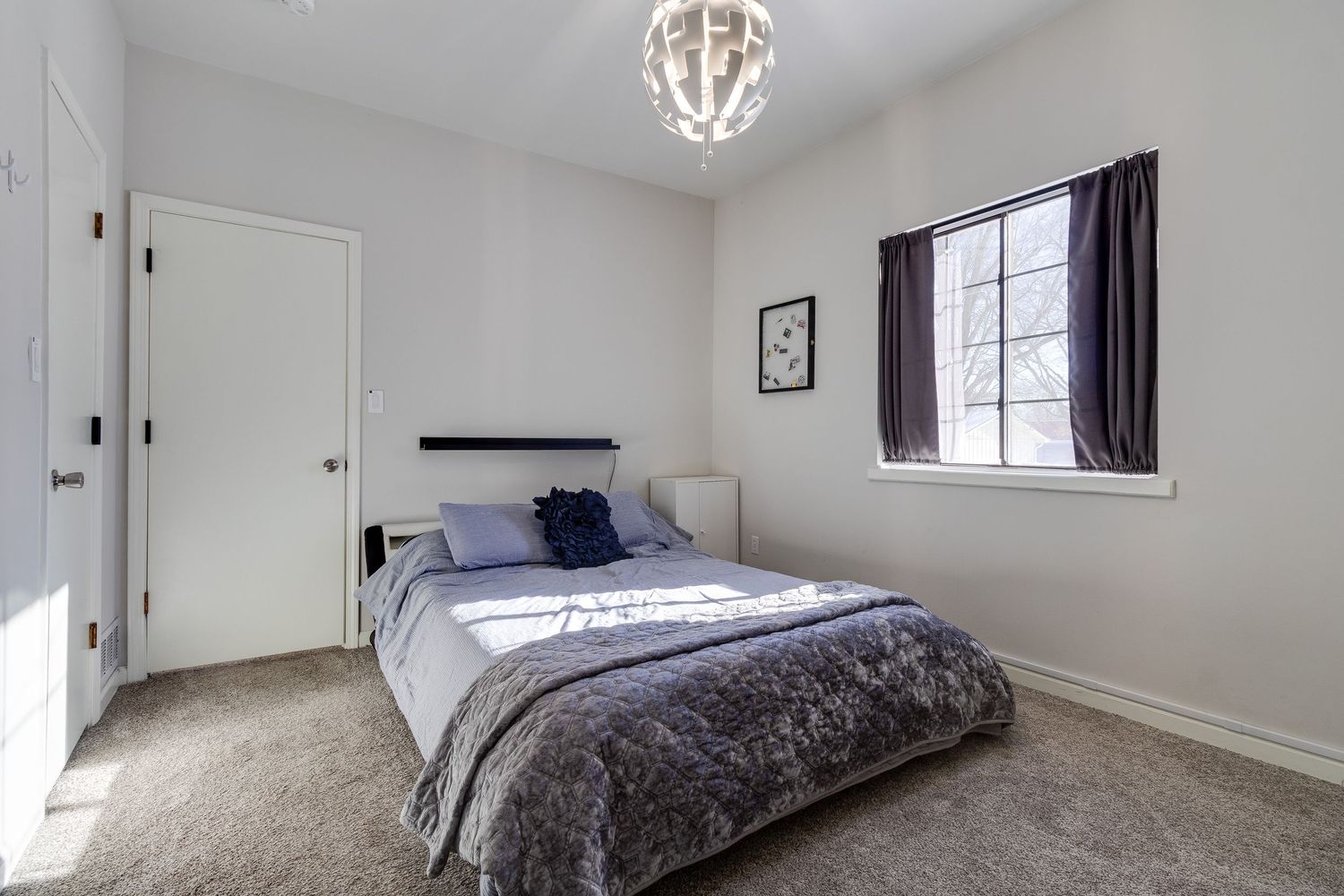 Cozy bedroom with gray bedding, decorative light fixture, and large window providing natural light.