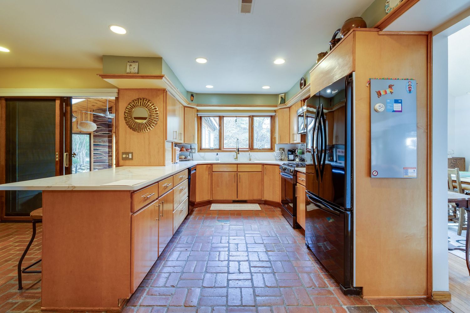 Spacious kitchen with terra cotta floors, wooden cabinets, and black appliances.