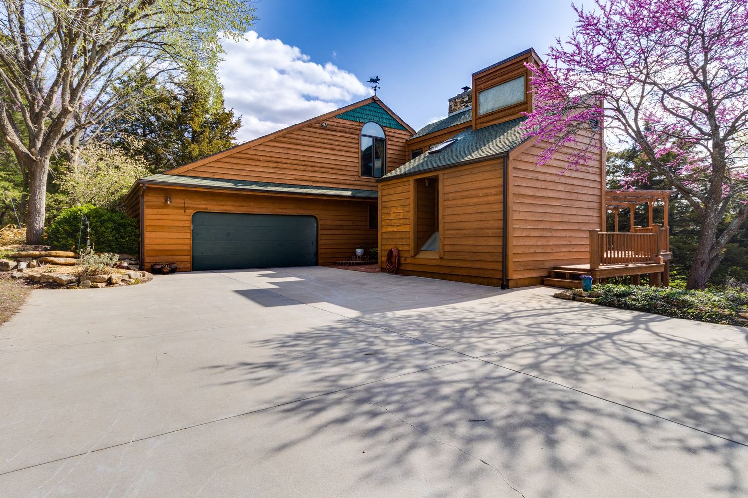 Modern wooden-sided house with a two-car garage and natural landscaping under blue skies.