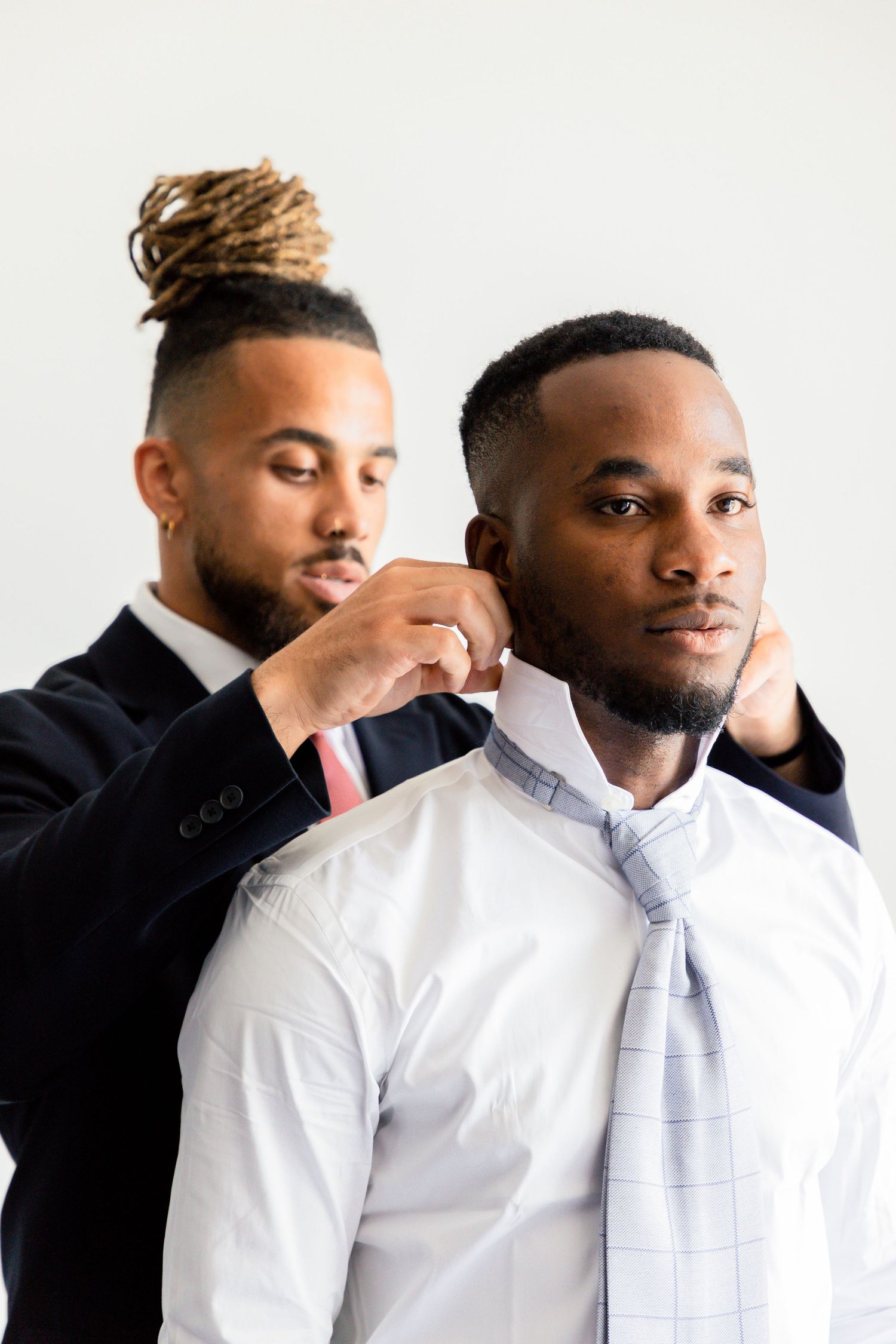 Series of portraits showing two men in formal white shirts and ties getting ready.