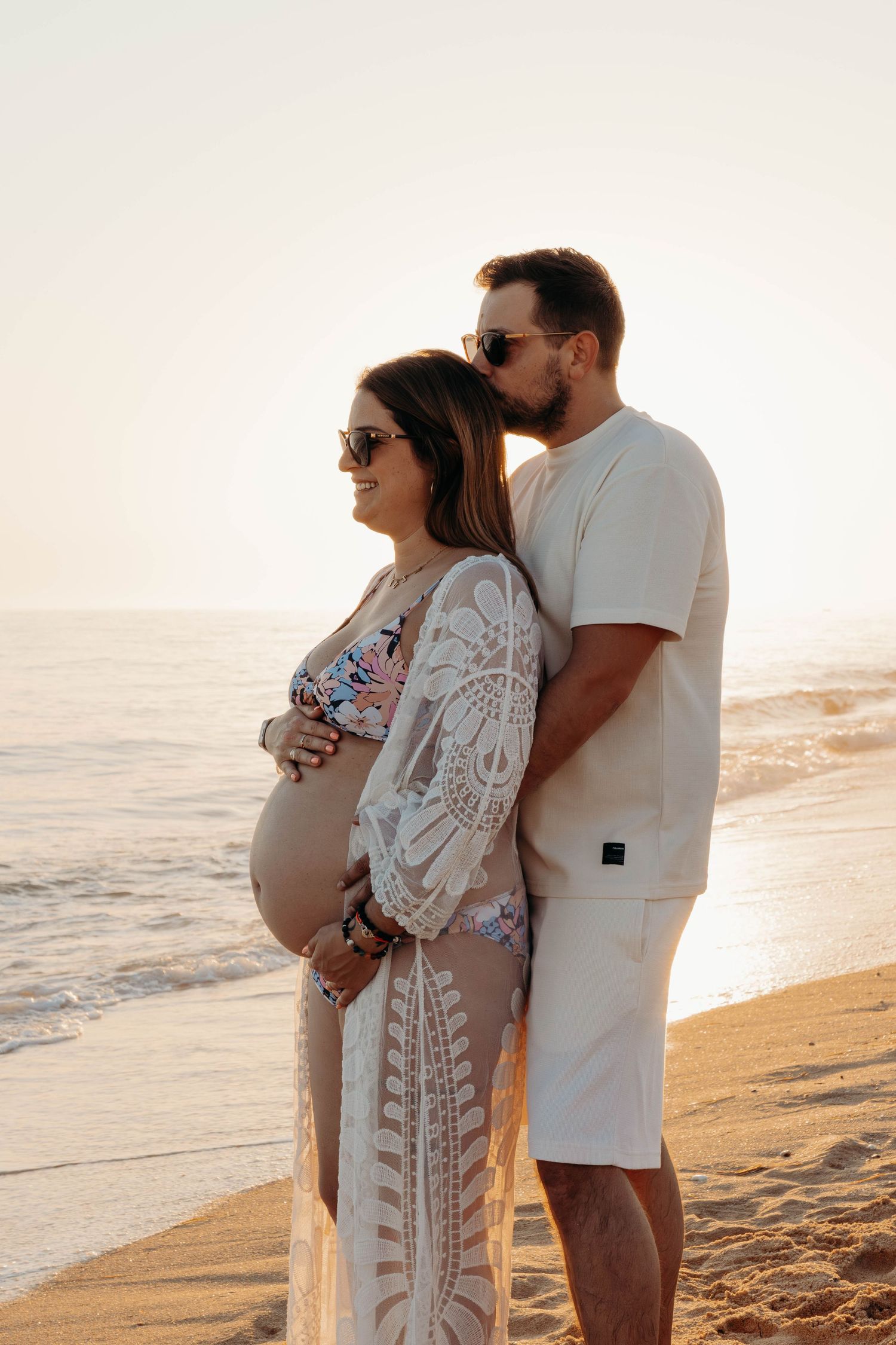 A romantic maternity beach photo with a pregnant woman in a lace coverup and her partner.