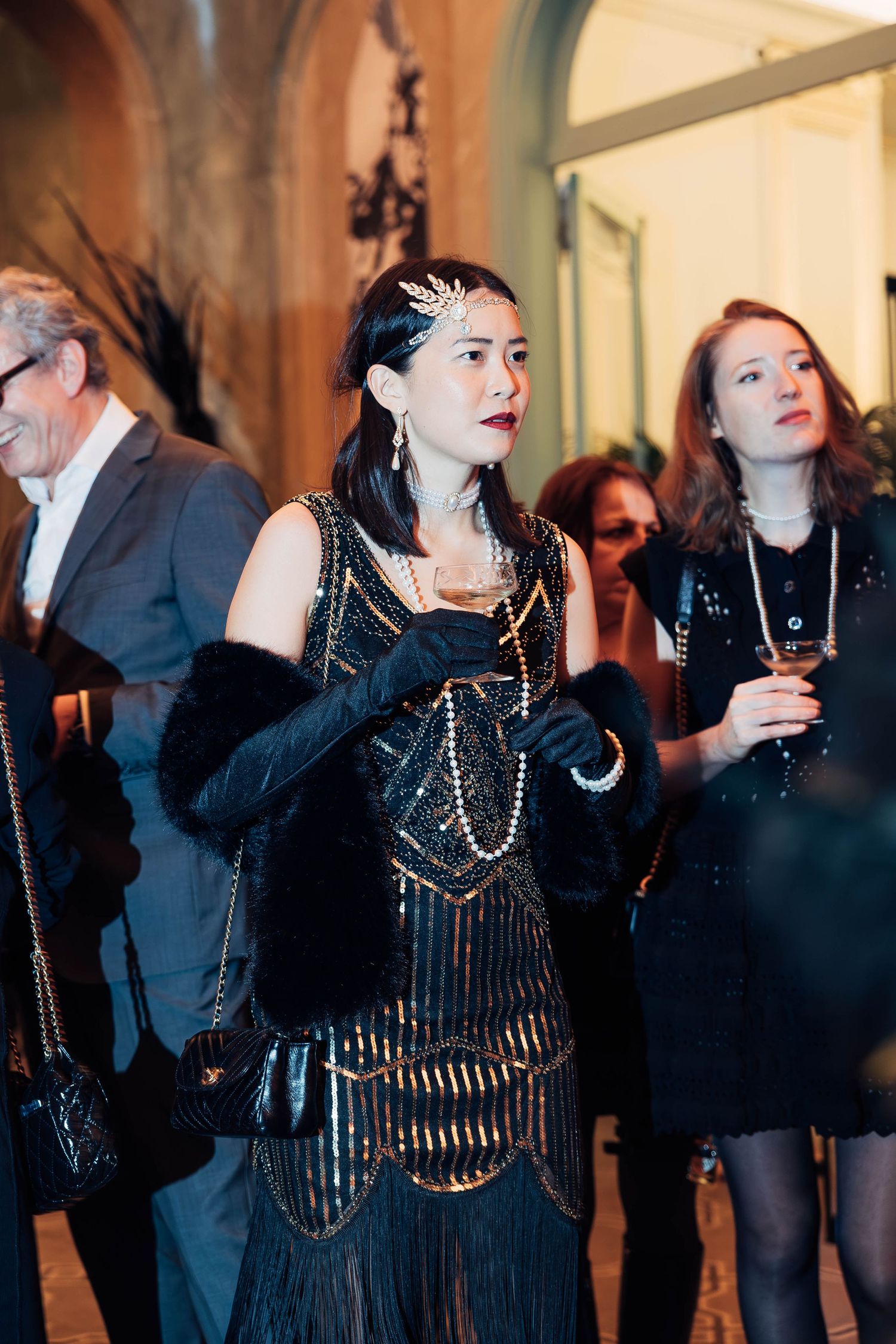Guests in formal black attire at a vintage-inspired party with art deco architectural details.