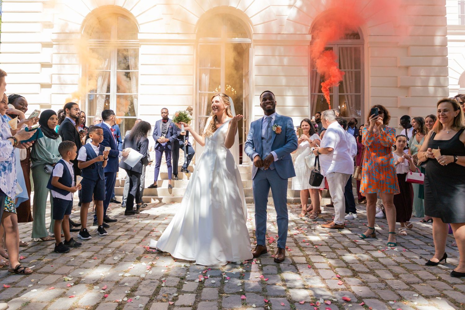 Wedding celebration photos with guests and colored smoke effects in a historic courtyard setting.