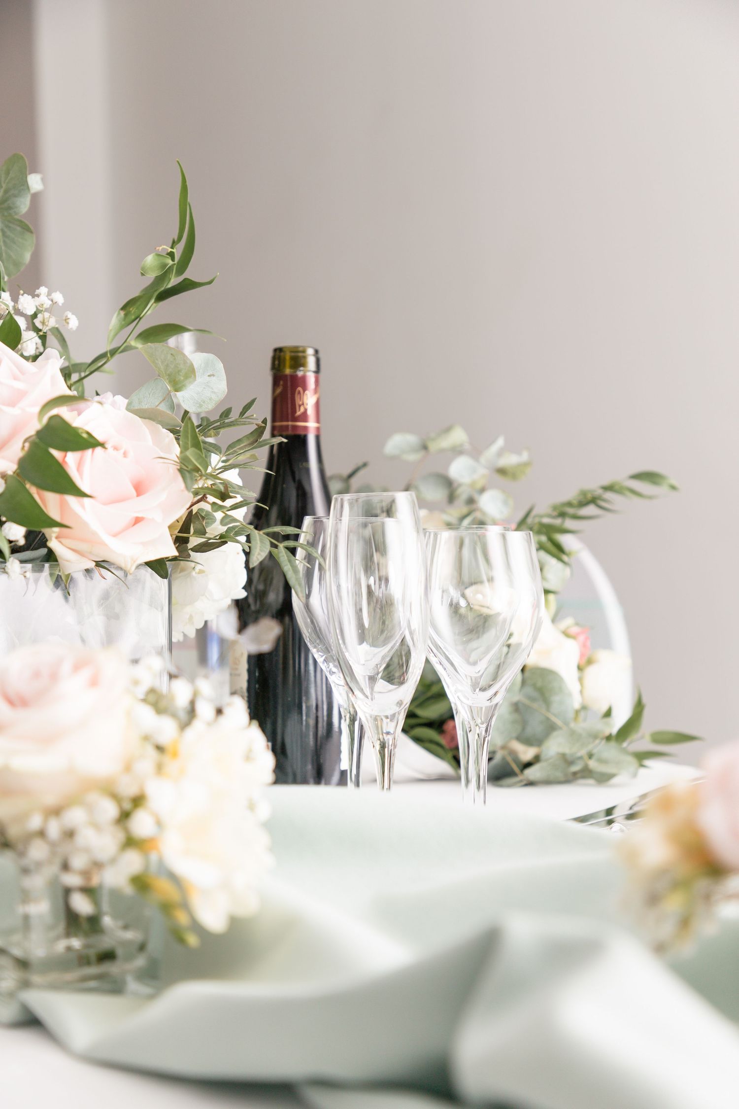 Elegant table setting with wine glasses, blush roses and eucalyptus centerpiece.