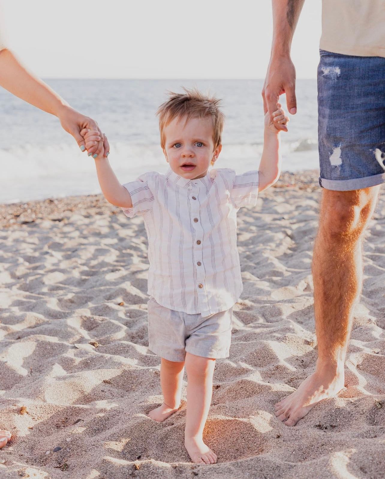 Close-up of small feet and hands in the sand during a family beach session.