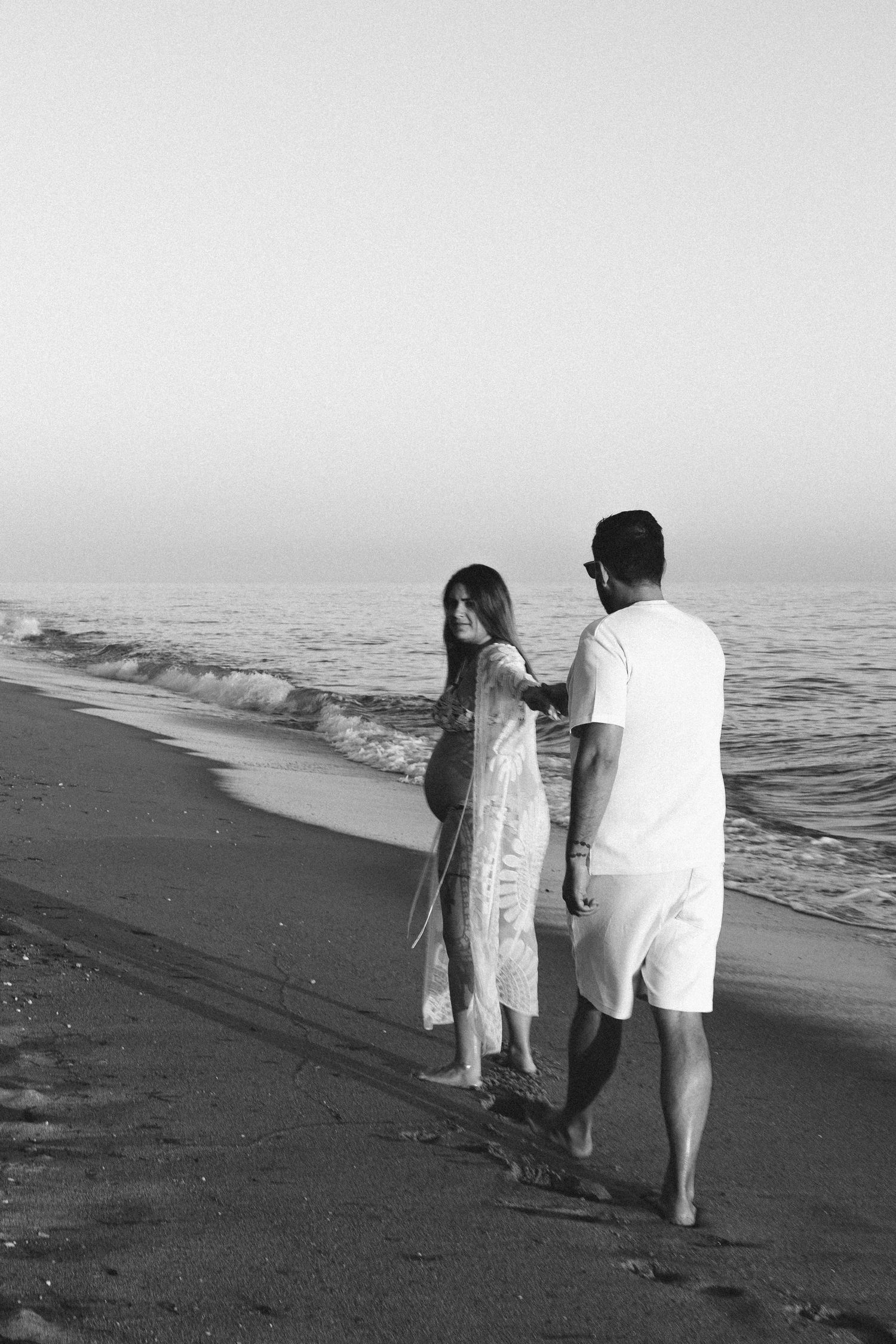 Black and white photo of a couple walking together along the ocean shoreline.