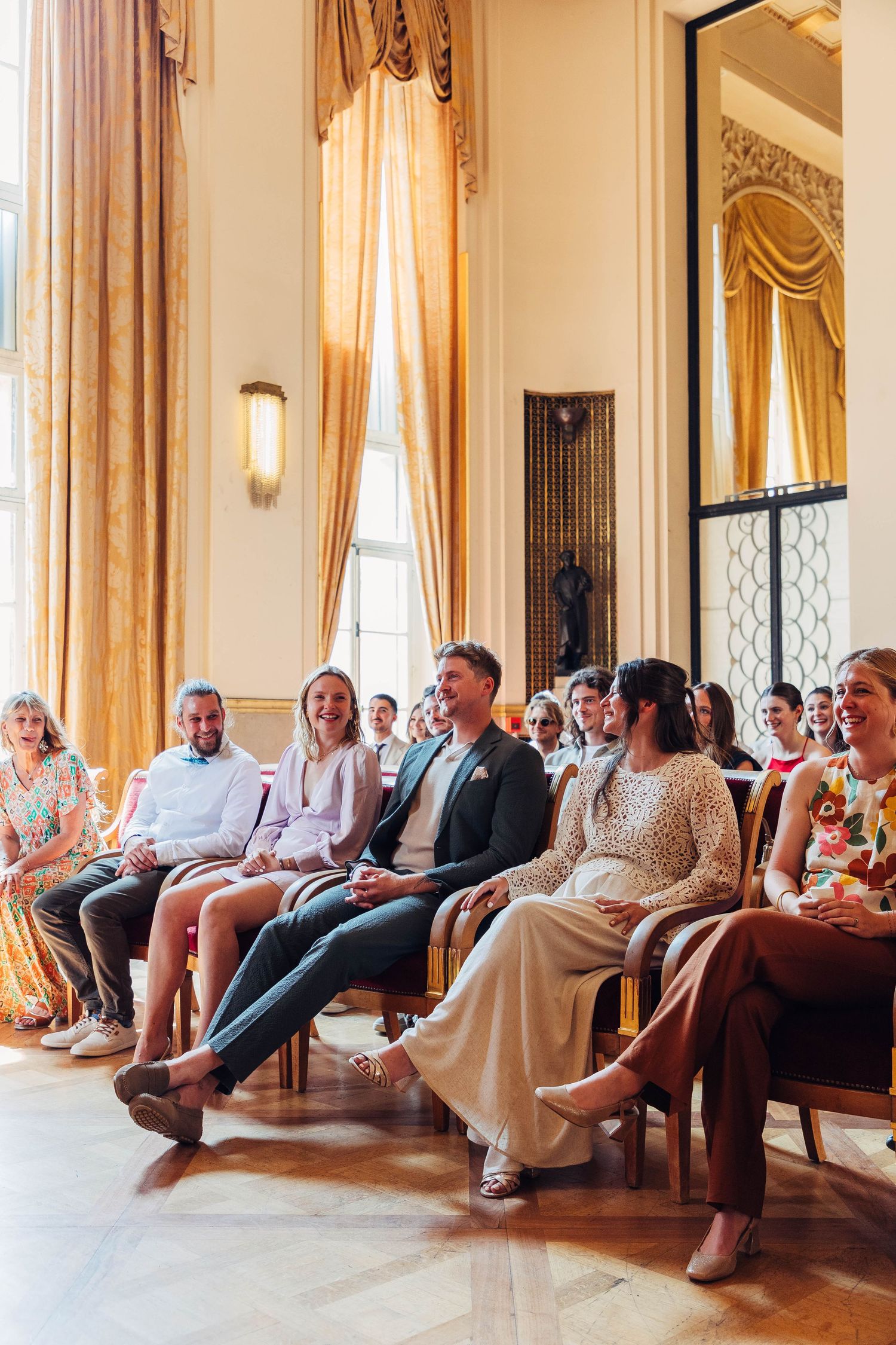Wedding guests seated in elegant room with golden curtains and ornate decor.