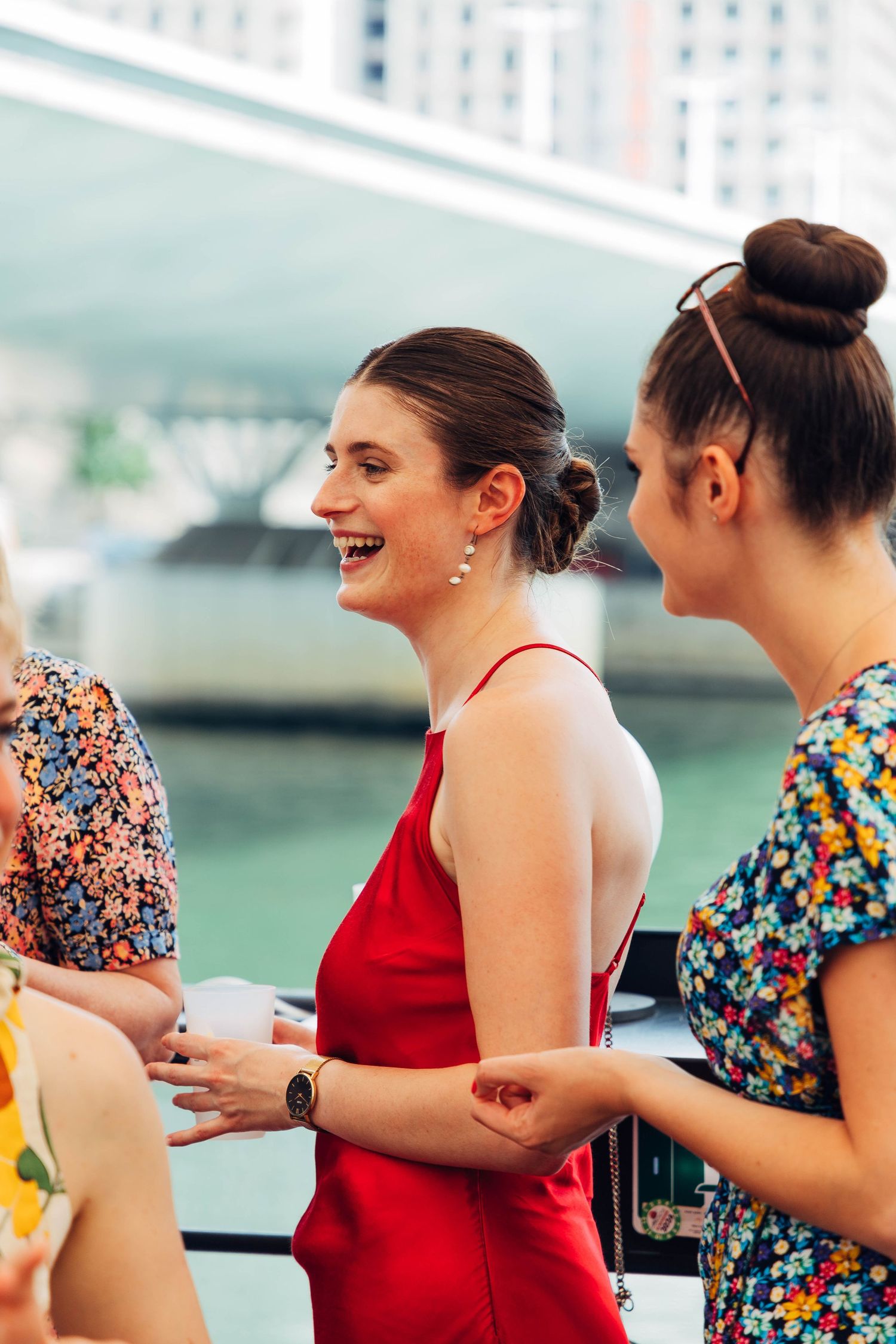 Women enjoying drinks and conversation on waterfront deck.
