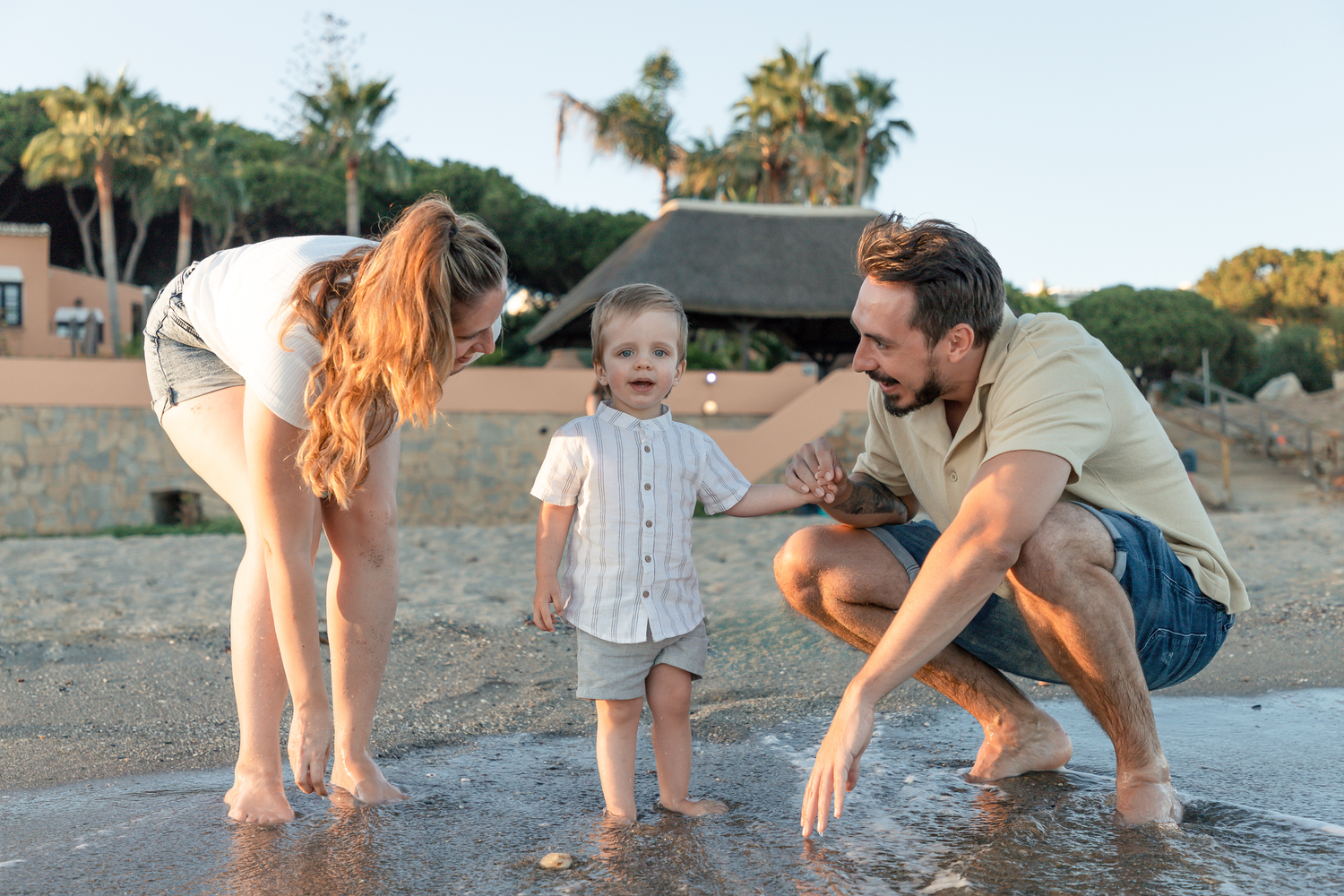 Family playing together on beach at sunset near palm trees.