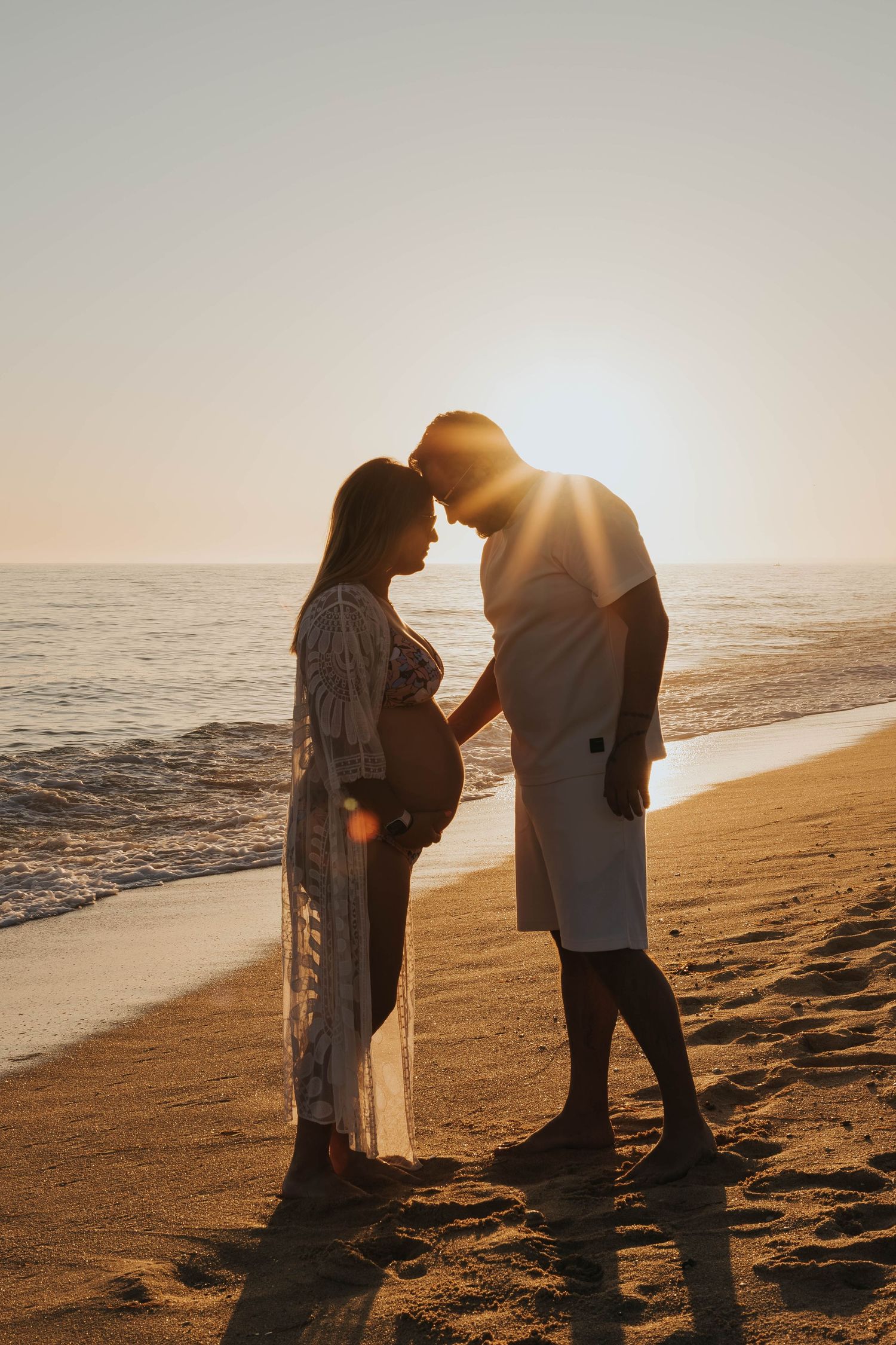 Silhouetted couple shares intimate moment on beach at golden hour.