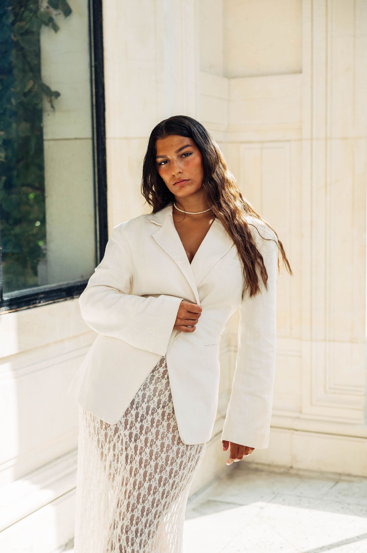 Elegant white blazer and lace dress combination photographed against classic architecture.