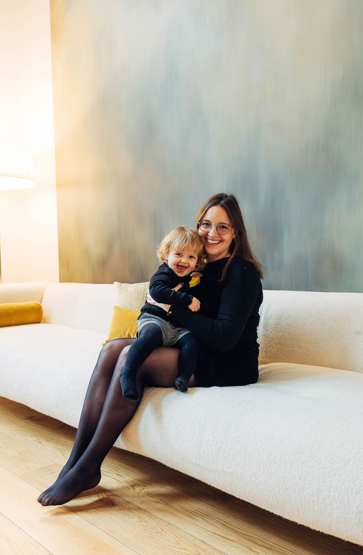 A parent and child share a tender moment while sitting together on a white sofa in a minimalist room.