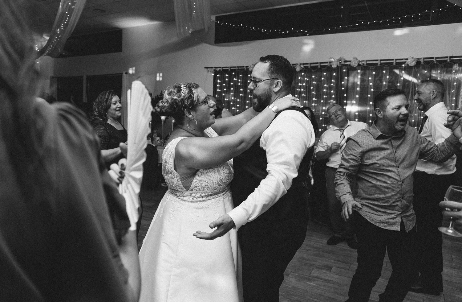 A couple shares their first dance at a wedding reception with twinkling lights in the background.