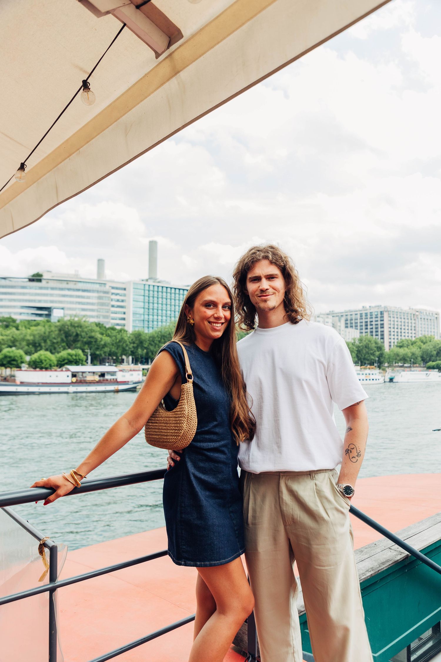 Couple posing on boat deck with city skyline in background.