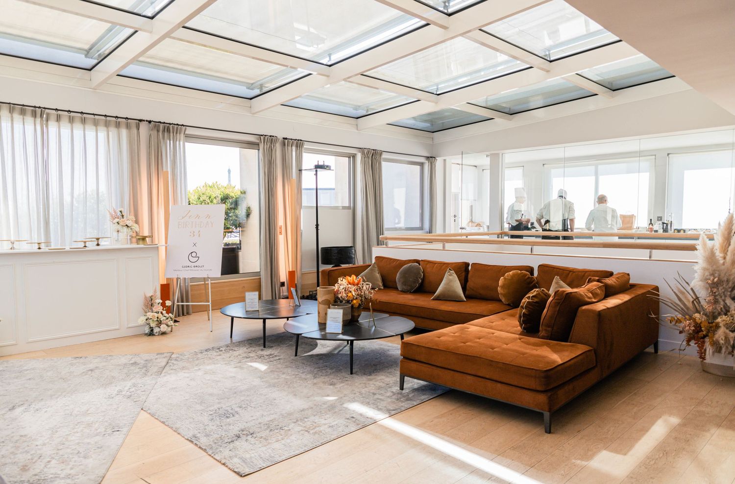 Modern living room with brown leather sectional sofa, skylights, and sheer white curtains in a bright sunlit space.