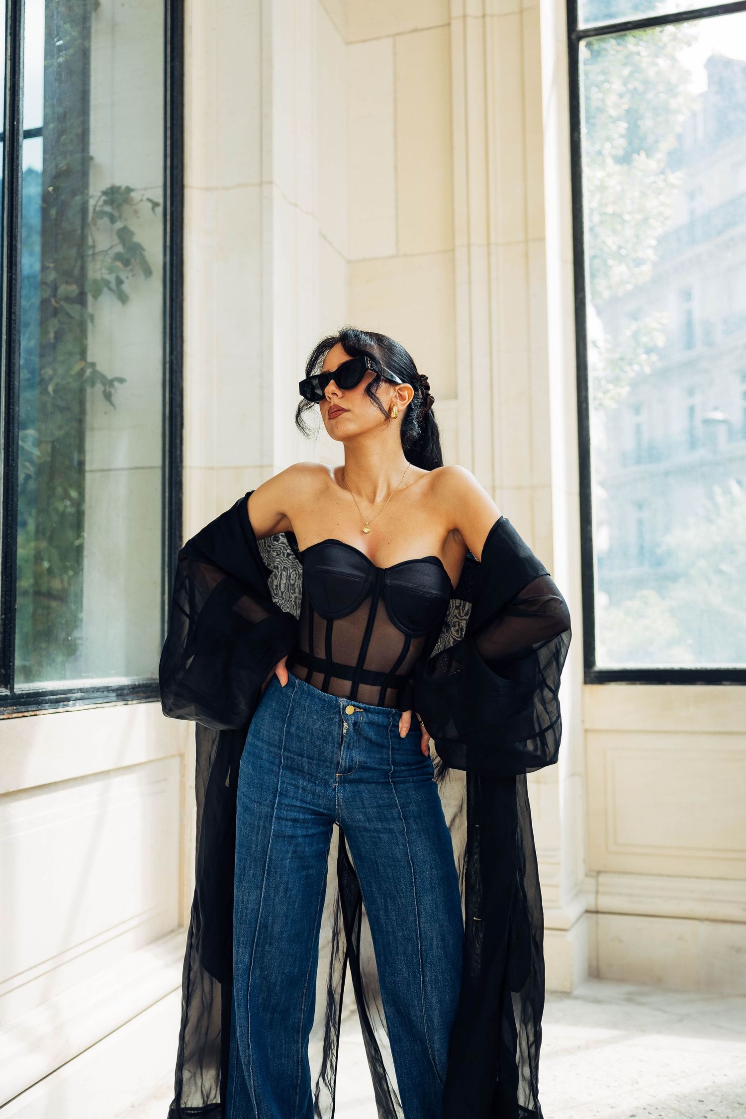 High fashion street style with black sheer coat, corset top and wide-leg denim jeans.