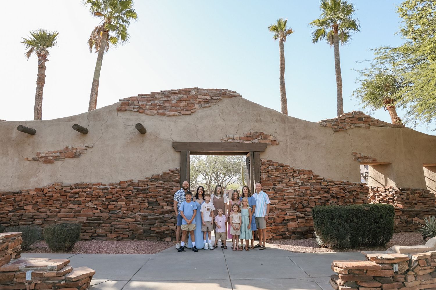 Family group photo in front of a rustic stone archway surrounded by palm trees in a desert landscape.