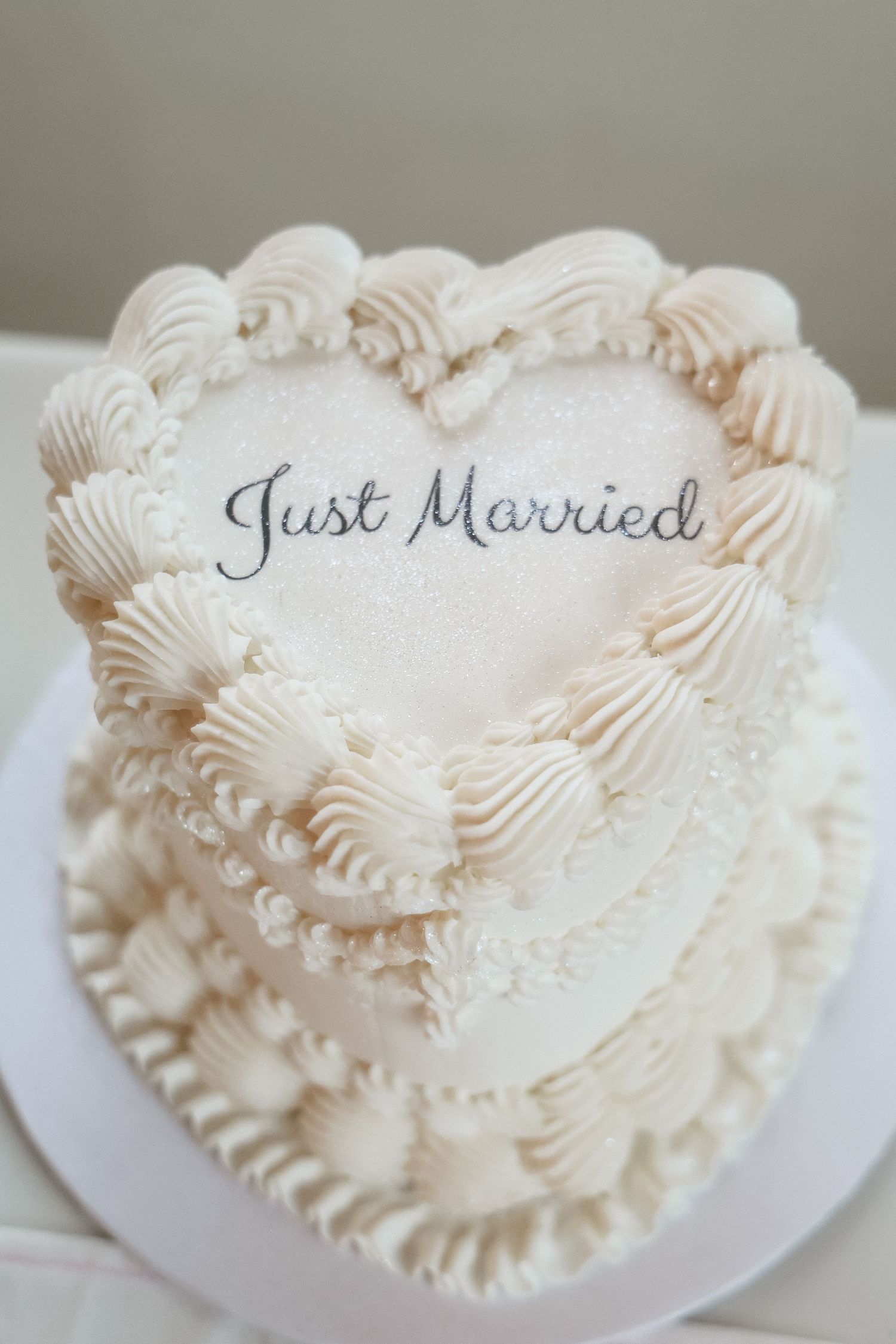 Elegant heart-shaped white wedding cake decorated with rosette piping and Just Married text on top.