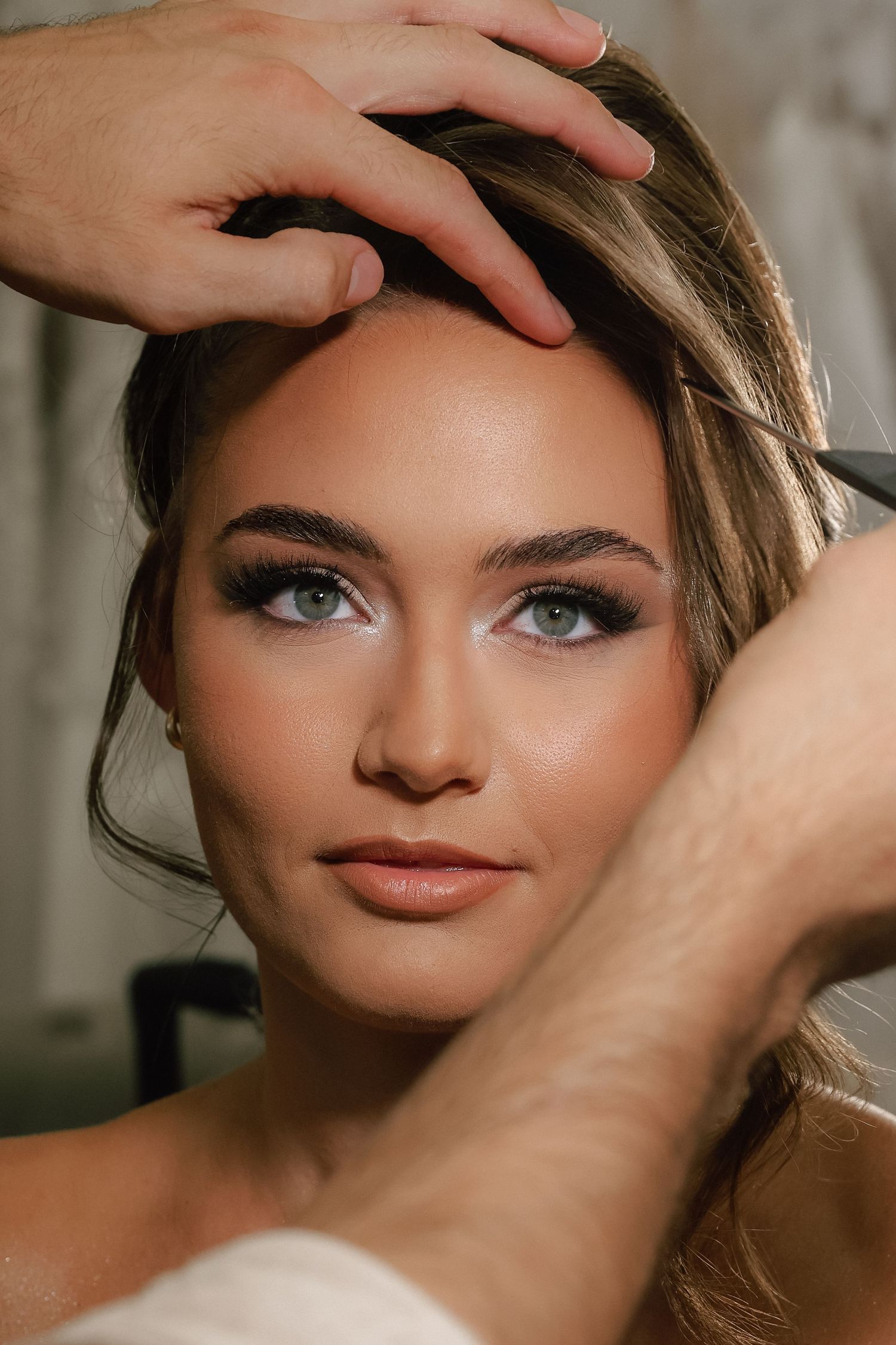 Close-up of a bride with smoky eye makeup and glowing skin being styled by a makeup artist.