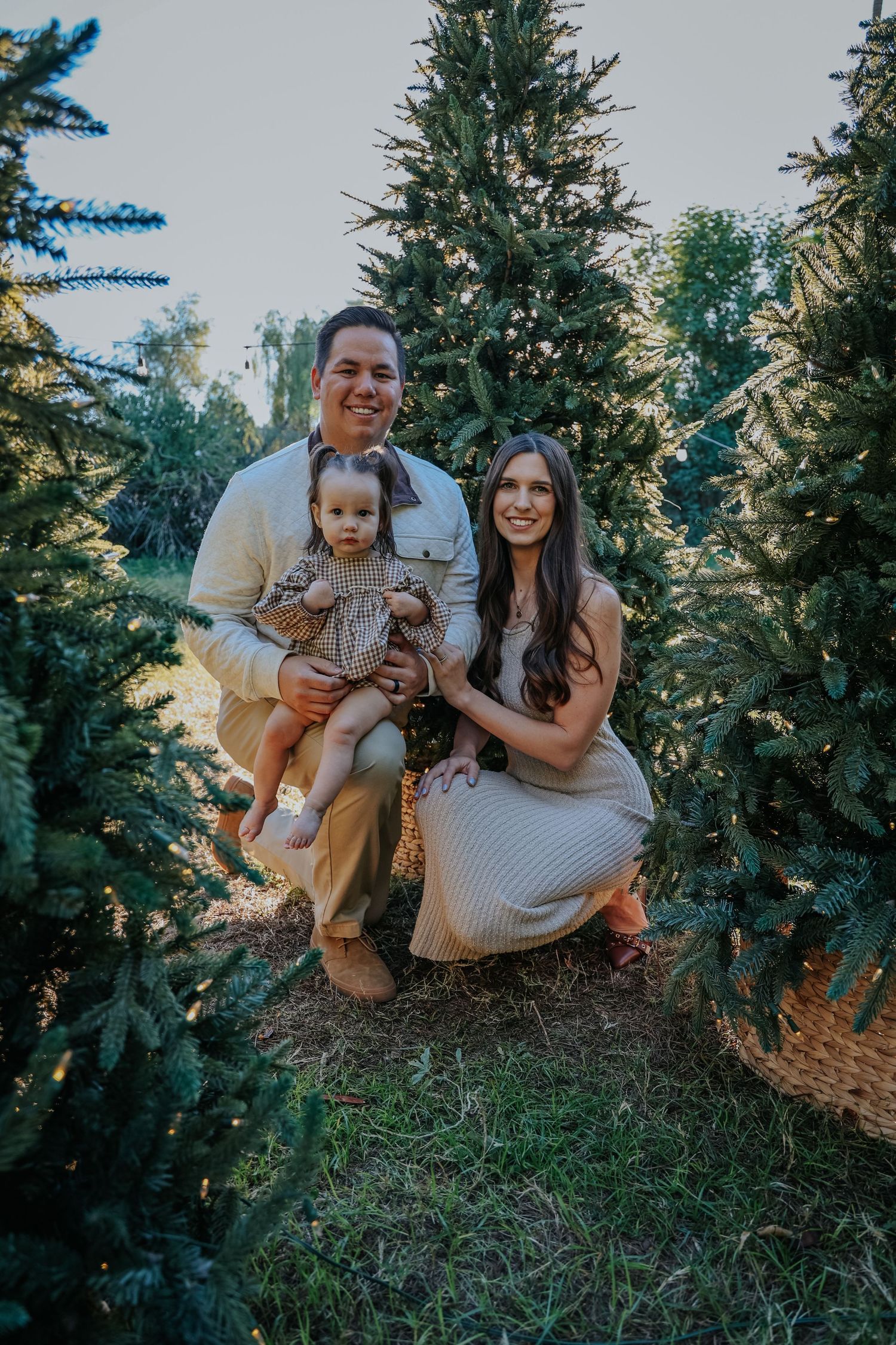 Family poses together among evergreen trees during outdoor photo session.