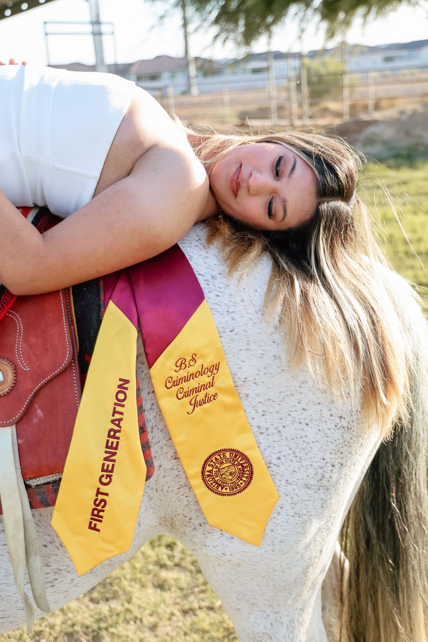 First generation graduate poses with graduation stoles on a white horse, wearing B.S. Criminology Criminal Justice sash.