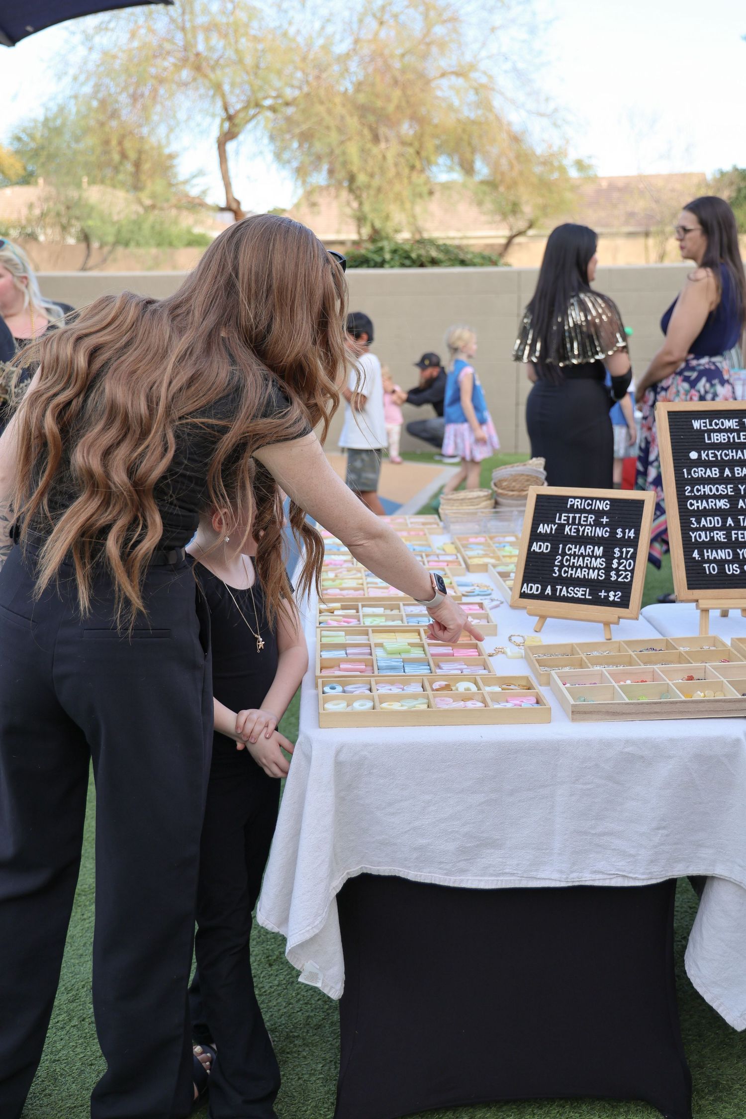 People browse items displayed on white tablecloths at an outdoor market or event.