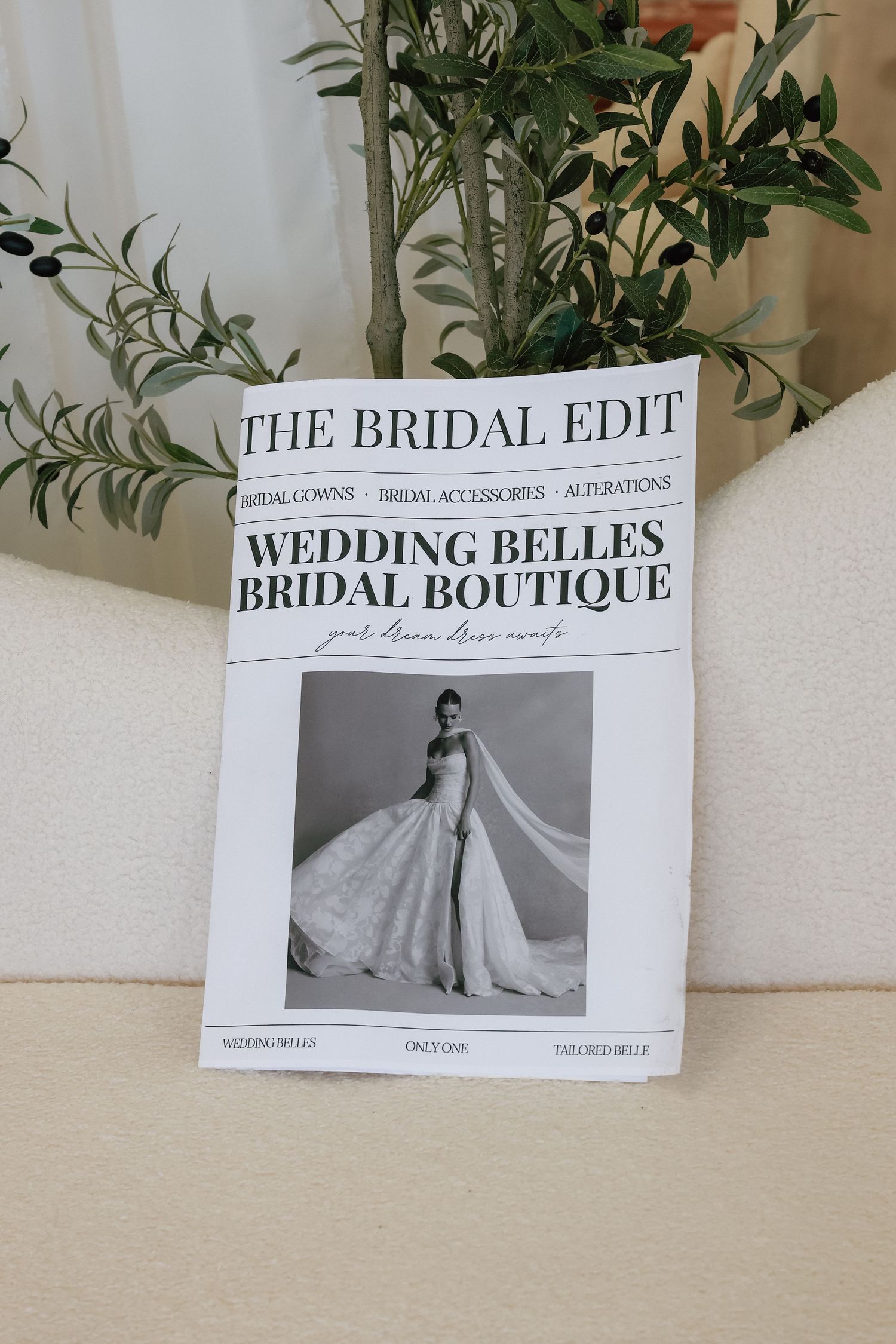Wedding Belles Bridal Boutique magazine-style brochure featuring a bride in a white gown, displayed on a cream chair.