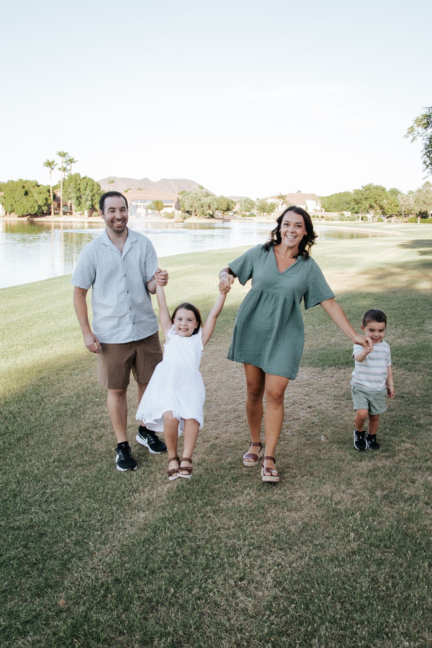 Family members walk together holding hands across a grassy field with mountains in background.