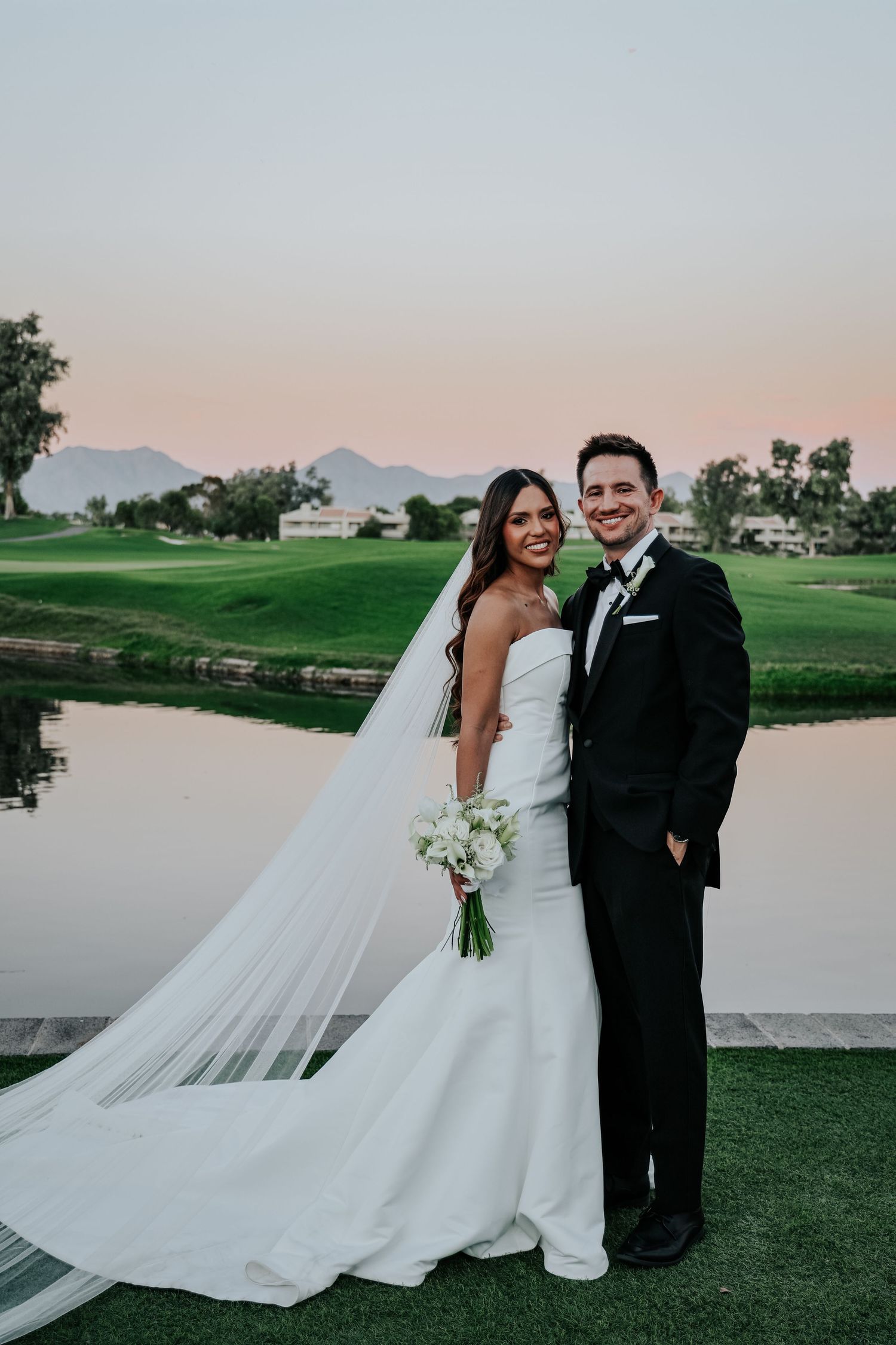 Wedding couple poses on a golf course at sunset with a flowing white dress and veil.