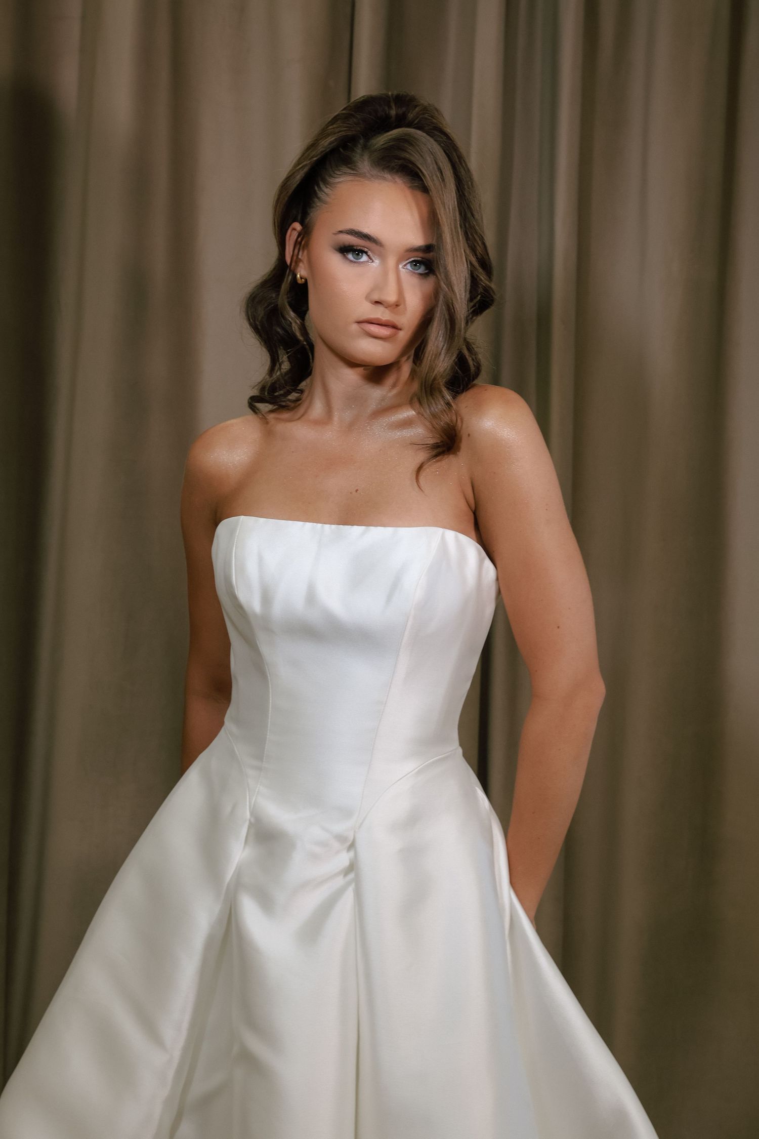 Elegant bride in a strapless white satin A-line wedding gown with a structured bodice, styled with soft curls.