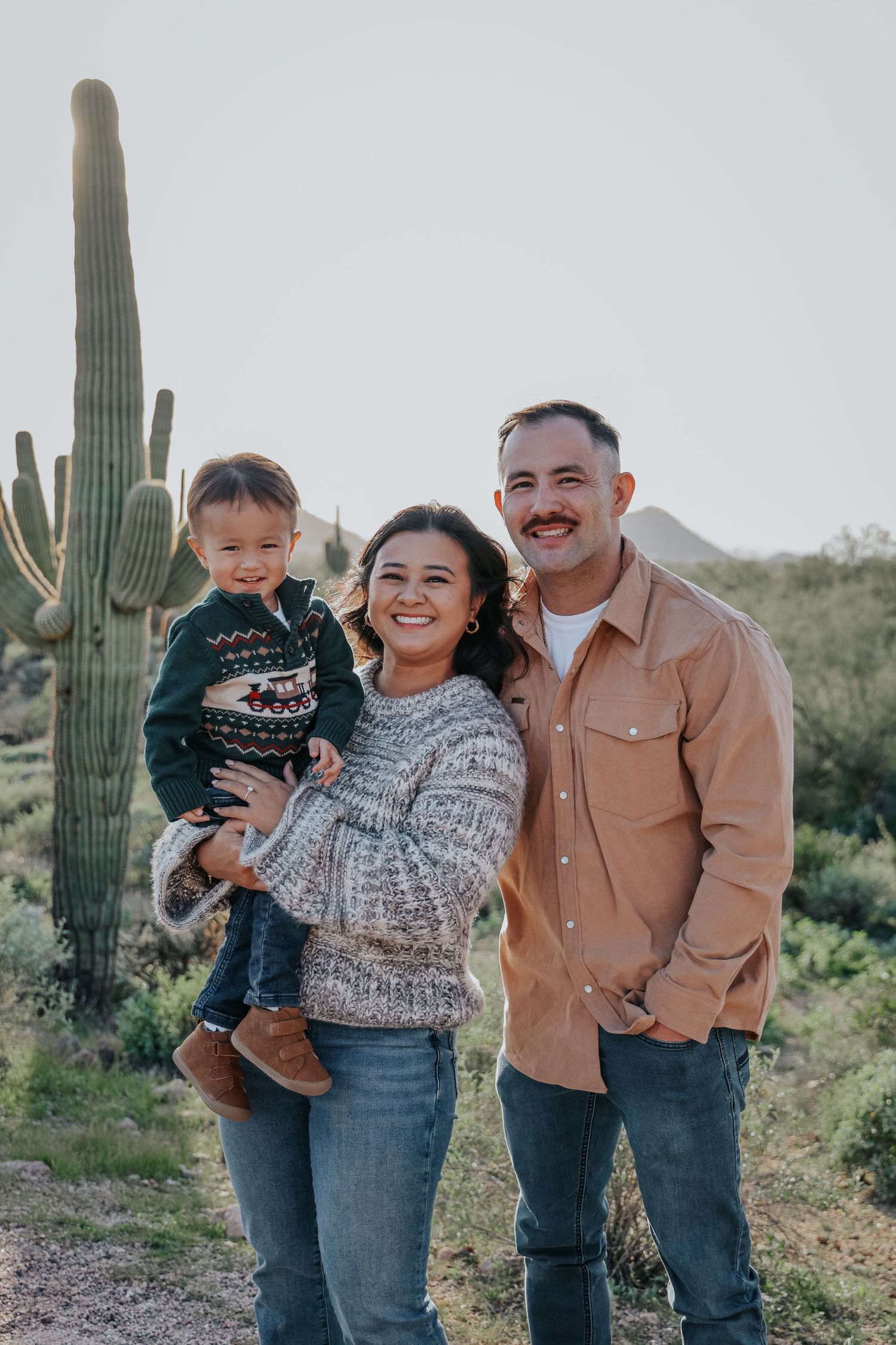 Happy family of three posing outdoors in Arizona desert with tall saguaro cactus in background.