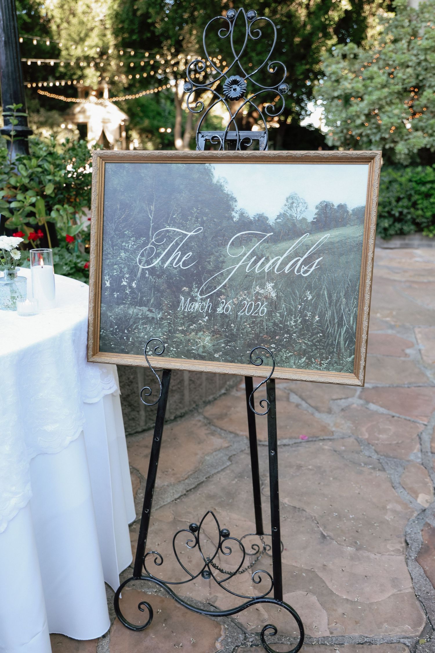 Elegant wedding welcome sign for The Judds on a decorative black easel at an outdoor garden reception venue.