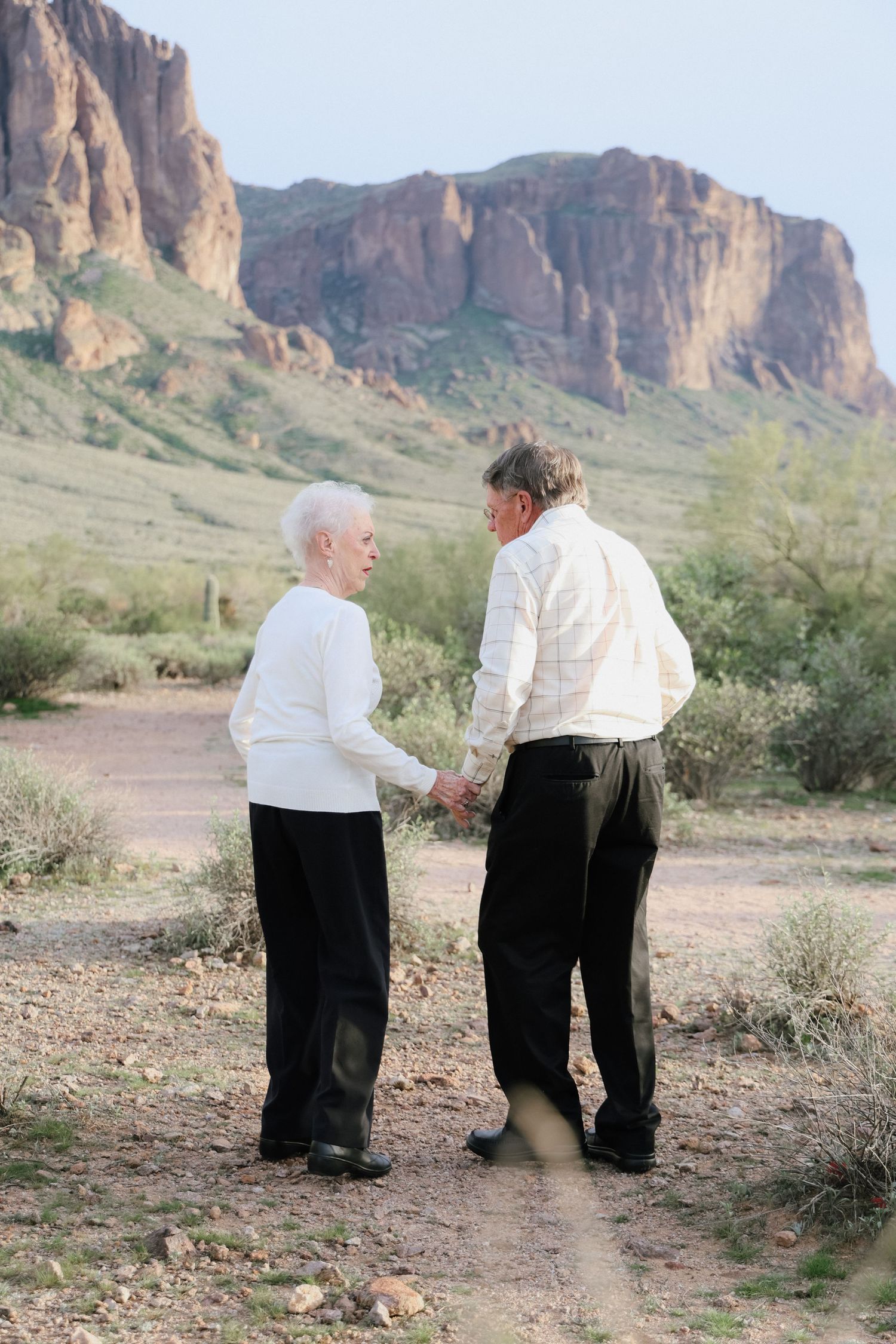 Couple sharing intimate moment on desert trail with Superstition Mountains in background.
