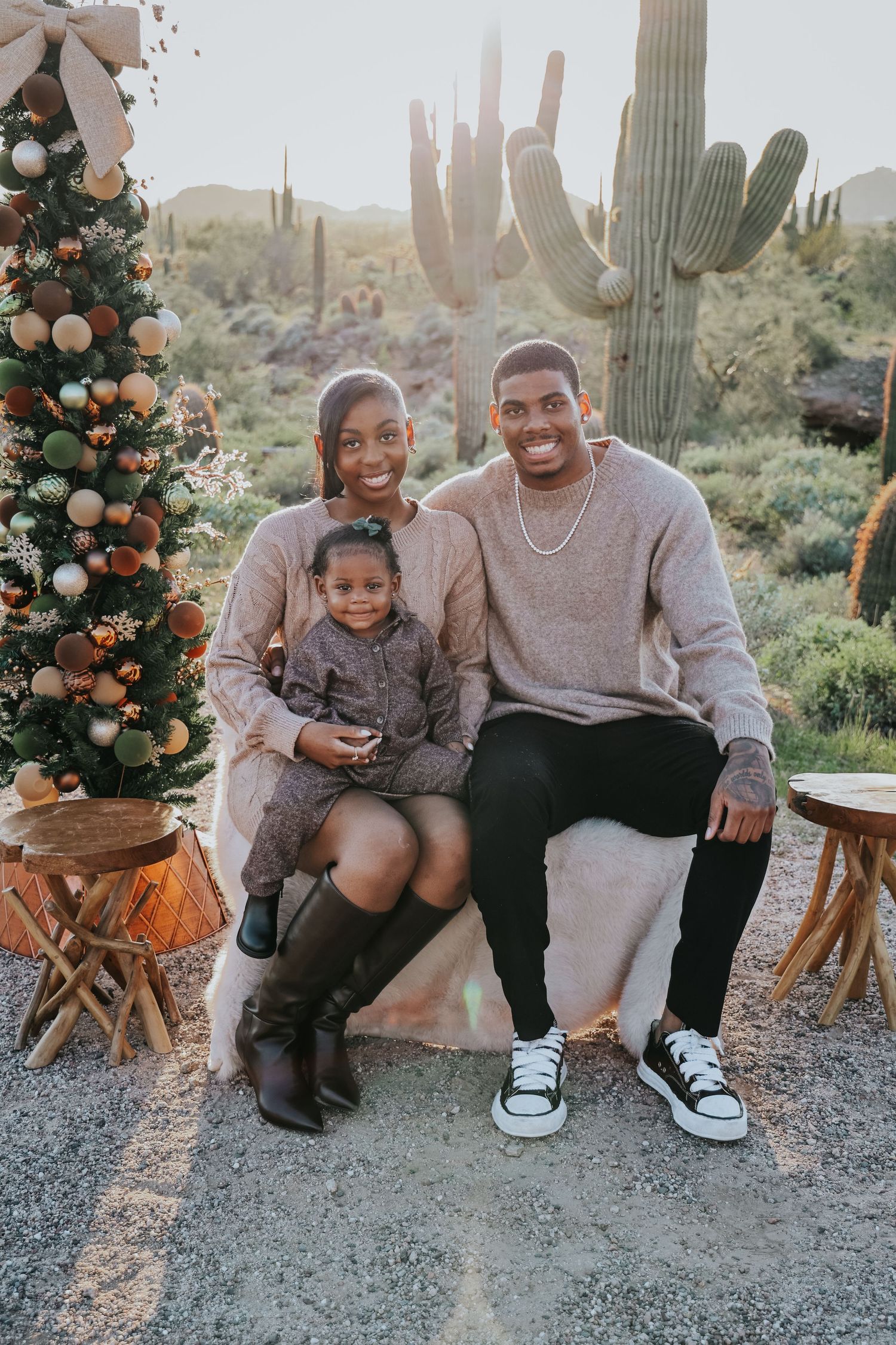 A family of three poses by a decorated Christmas tree in the Arizona desert with saguaro cacti in the background.