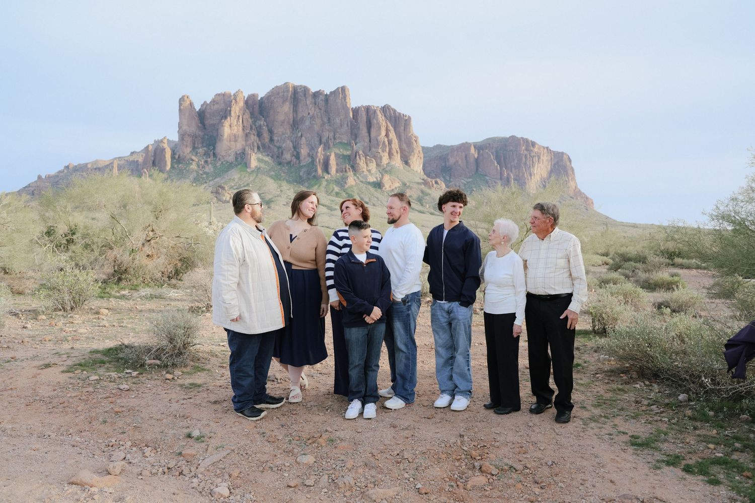 A group gathers in the desert landscape with rugged mountains and saguaro cacti in the background.