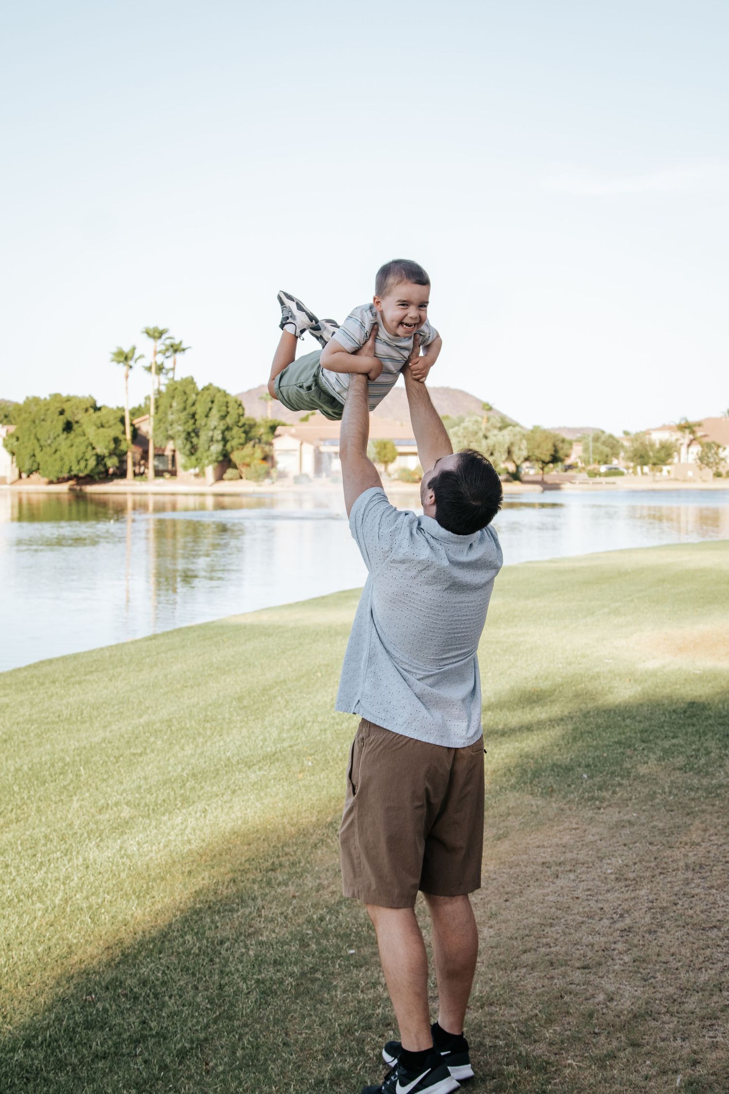 Playful family moments captured as parent lifts child in the air by a lakeside.