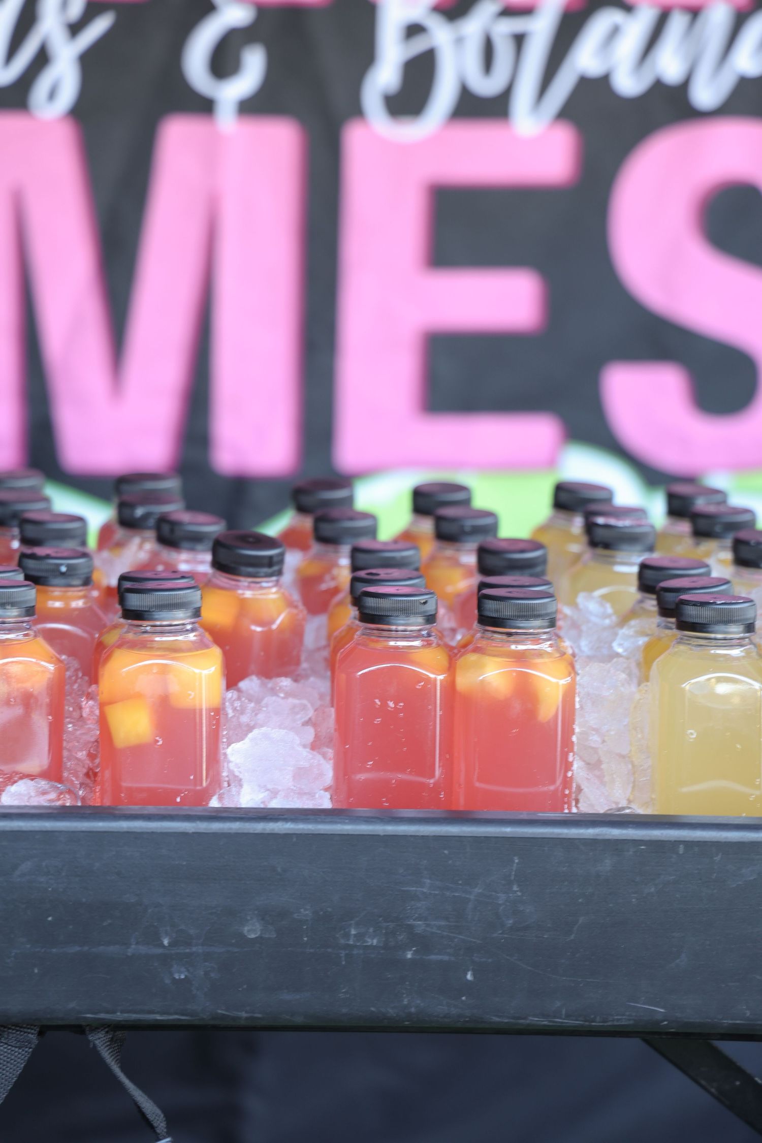 Colorful bottled beverages displayed in a row on ice at an outdoor event.