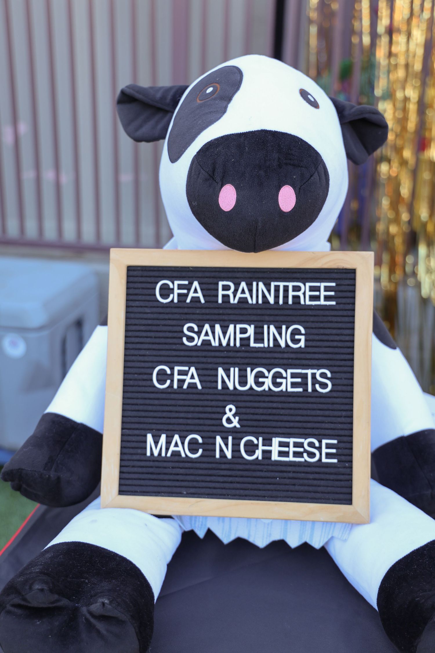 Chick-fil-A menu board signs showing items like Raintree, Mac n Cheese, and Nuggets with cow mascot plush toys.