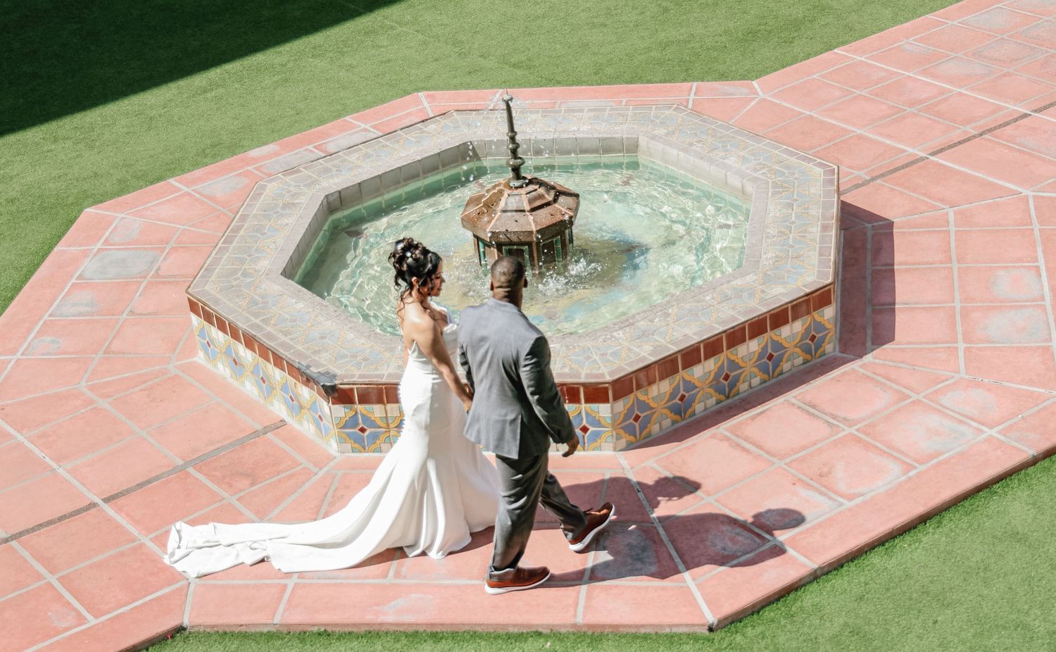 A couple poses for wedding photos near a brick fountain in a garden setting.