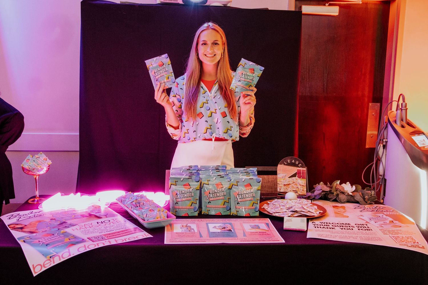 Pink-lit product display table with gift boxes and merchandise arranged for presentation.