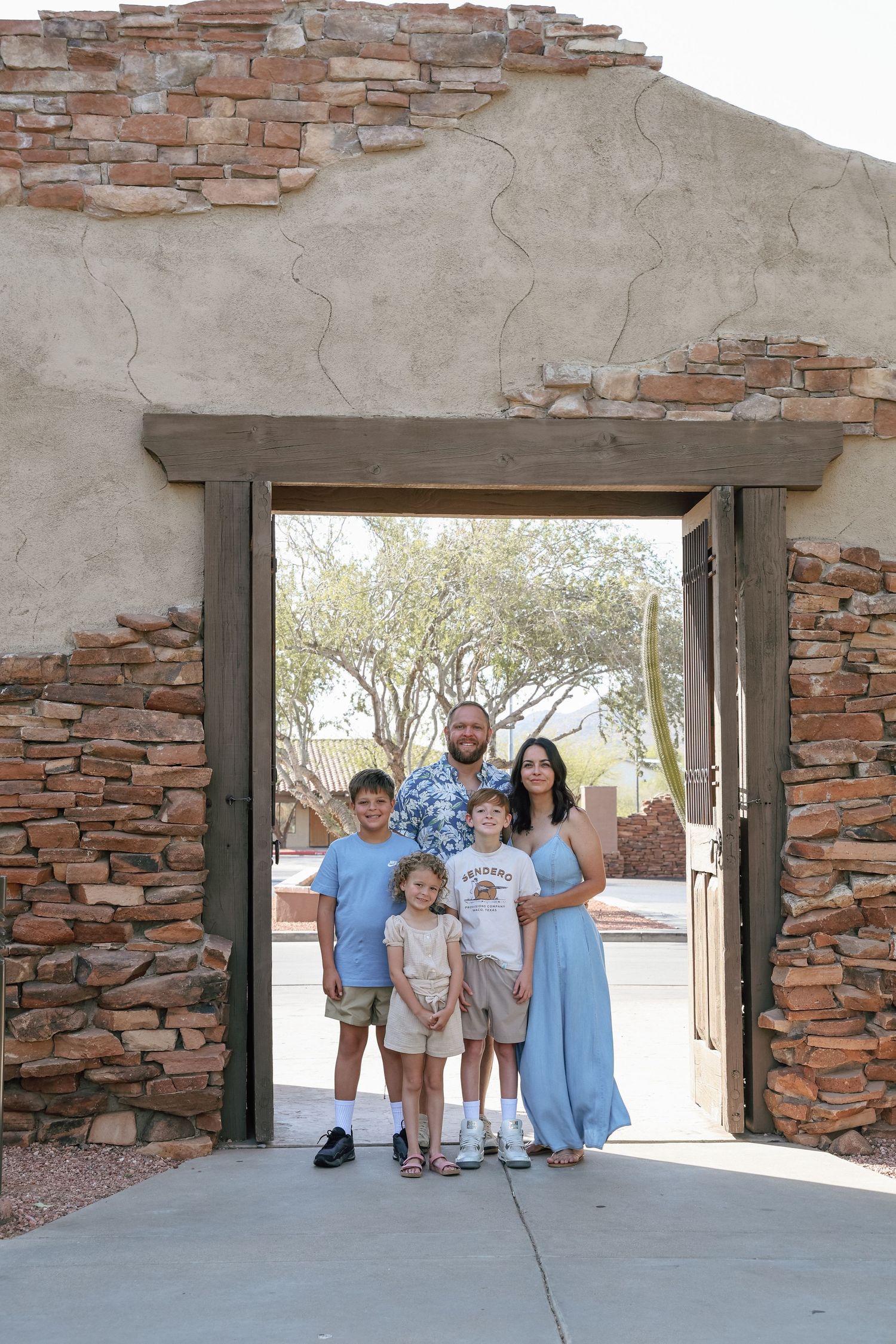 Family of five posing in a rustic stone archway doorway in an Arizona desert landscape setting.
