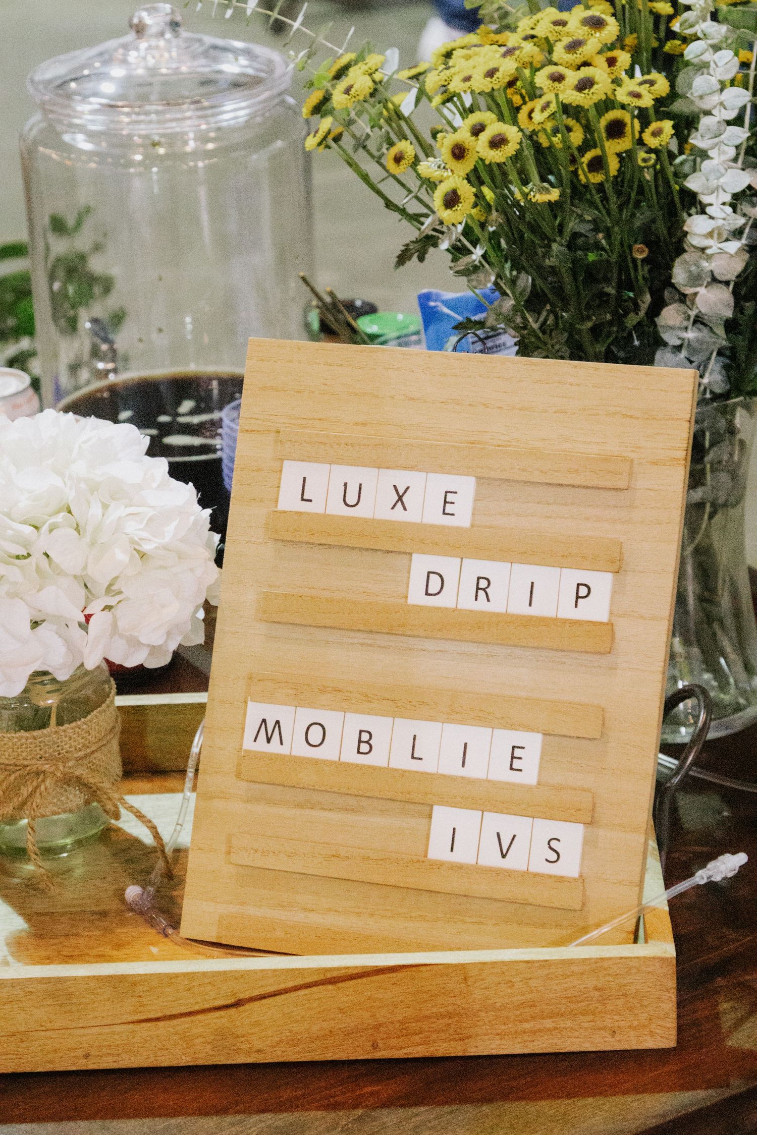 Wooden letter tiles spelling words displayed on stands with yellow flowers and white decorations in background.