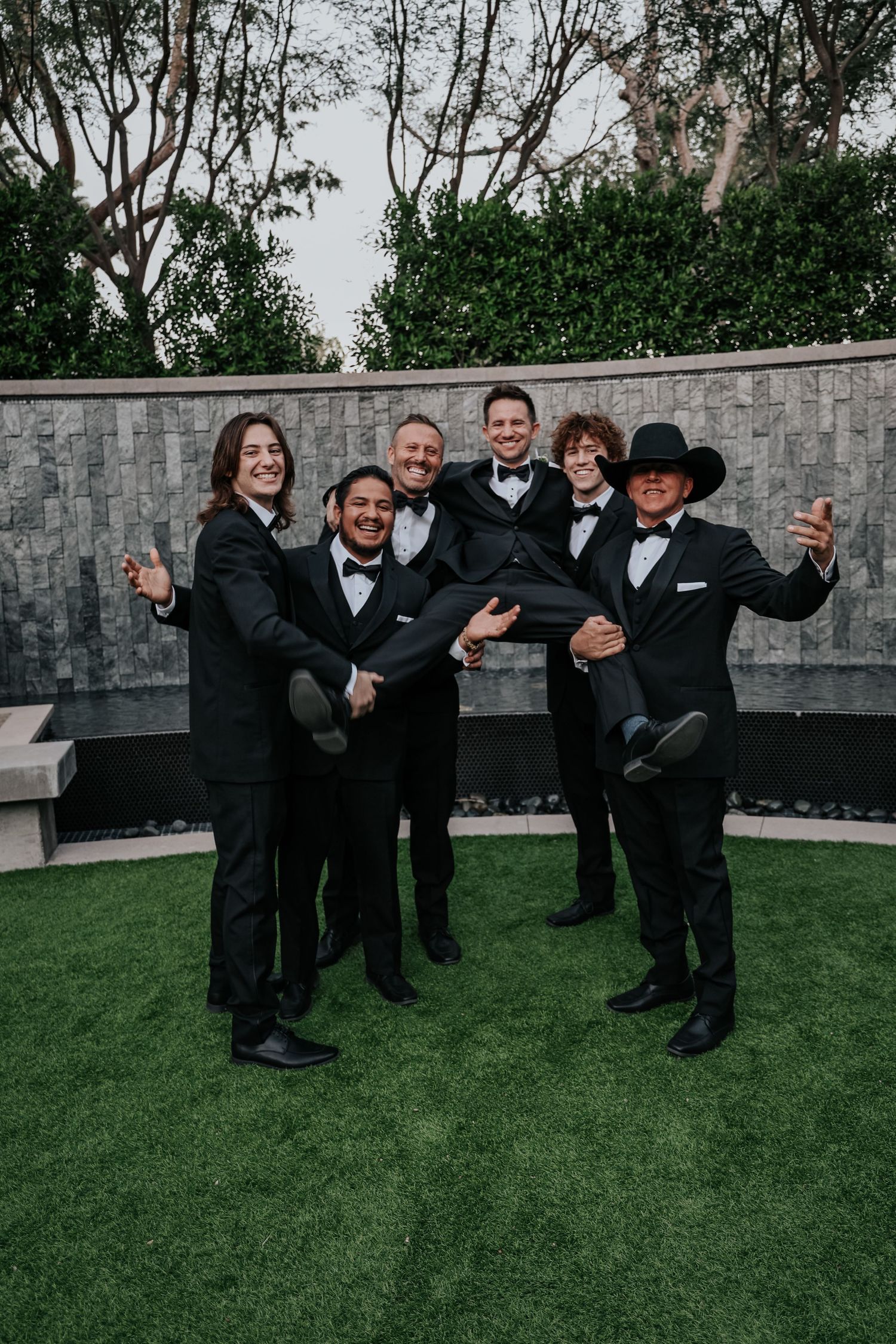 Groomsmen perform fun group poses on lawn during wedding photo session.