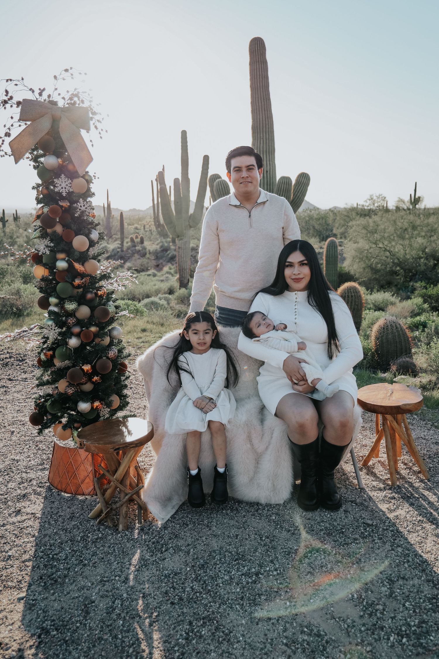 Family of four posing near a decorated Christmas tree and tall saguaro cacti in a desert landscape.