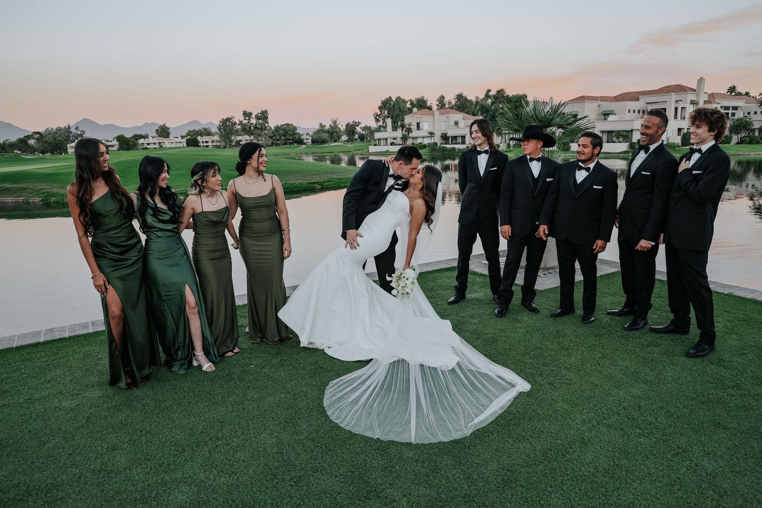 Wedding party lines up for formal photos on golf course during evening reception.