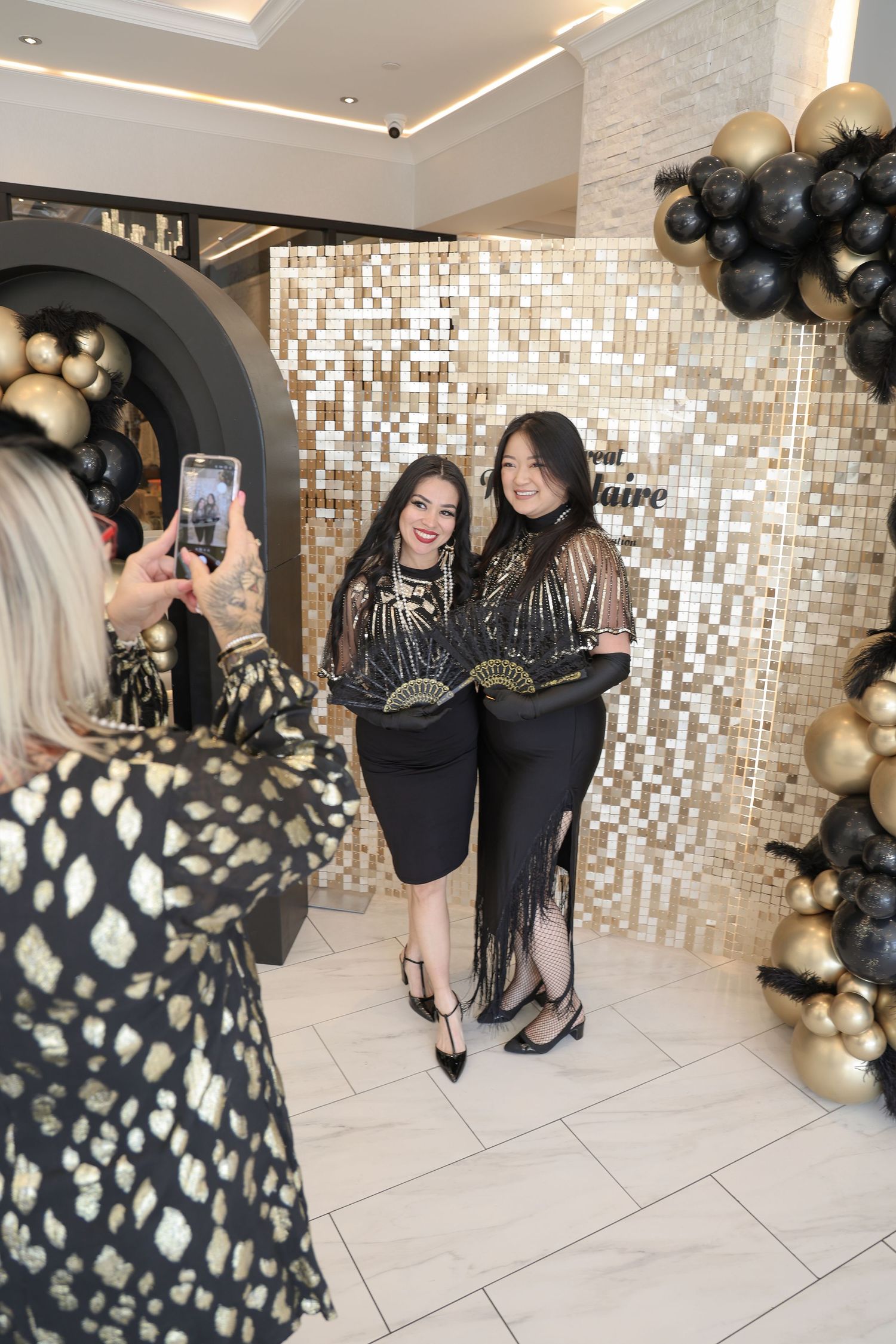 People in black and gold attire gather at an elegant event with mosaic walls and balloon decorations.