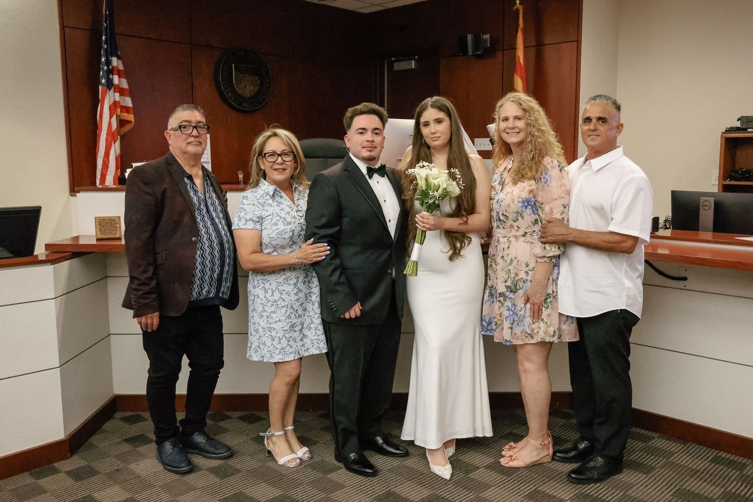 Group of six people posing together at a formal wedding ceremony in a courthouse setting.